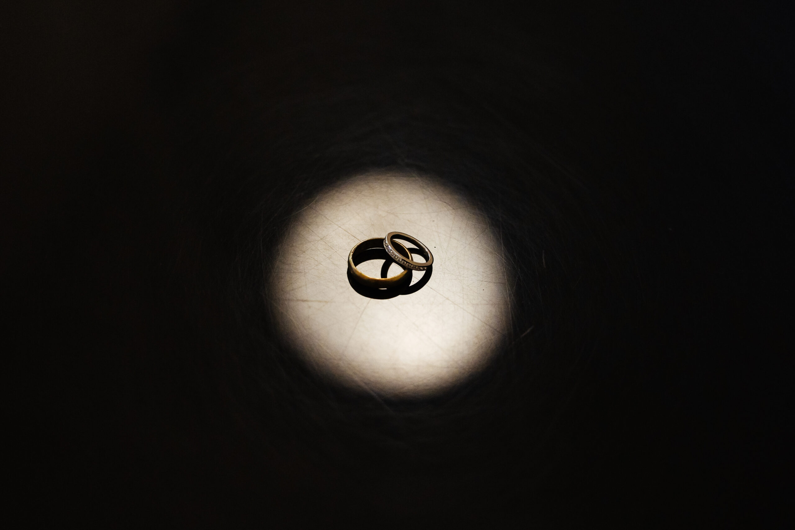 An image of two rings; one on top of the other and it is illuminated in a spotlight. The rest of the image is black.