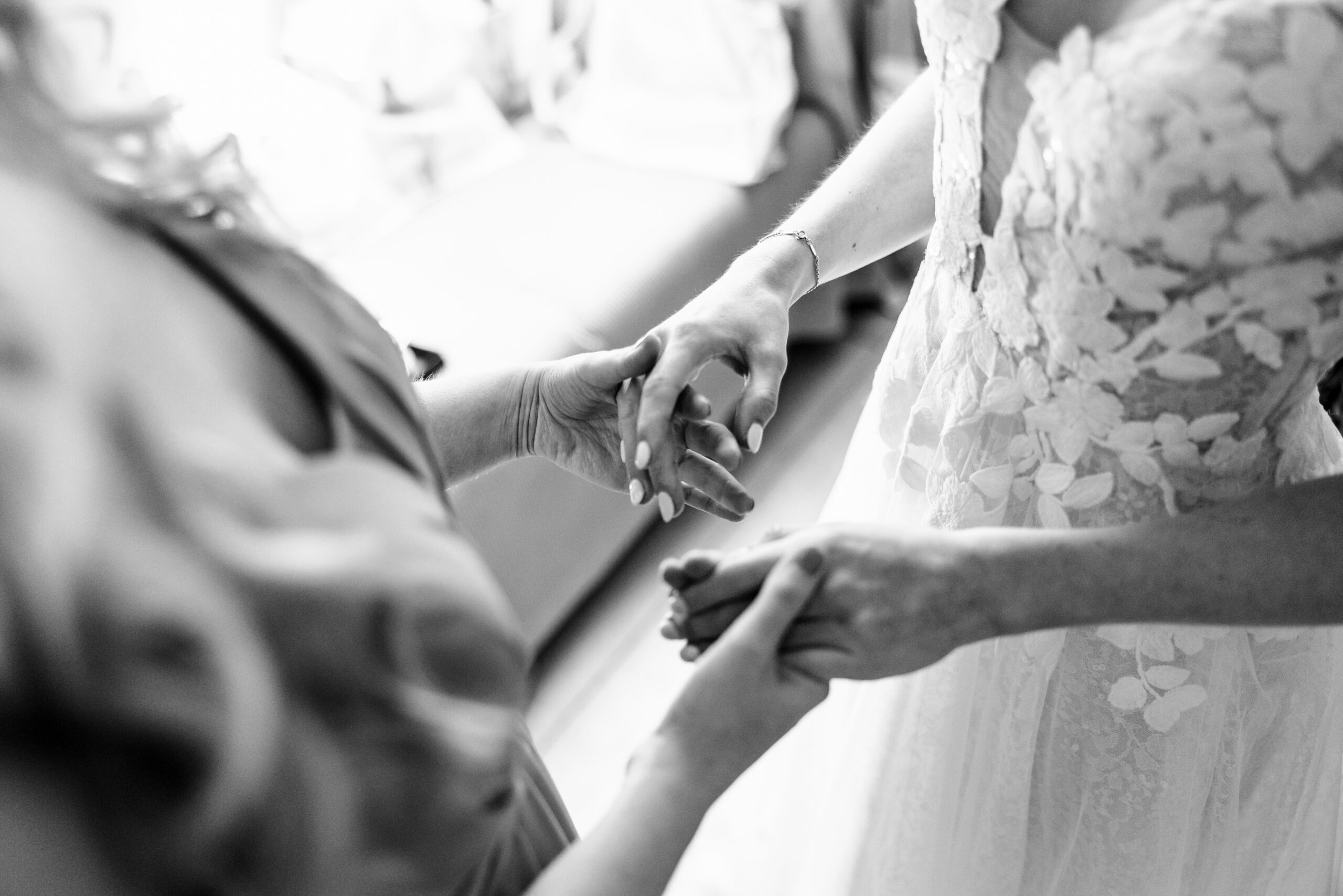 A mother and daughter holding hands. The bride has her detailed, lace wedding dress on and her mother has her wedding attire on too.