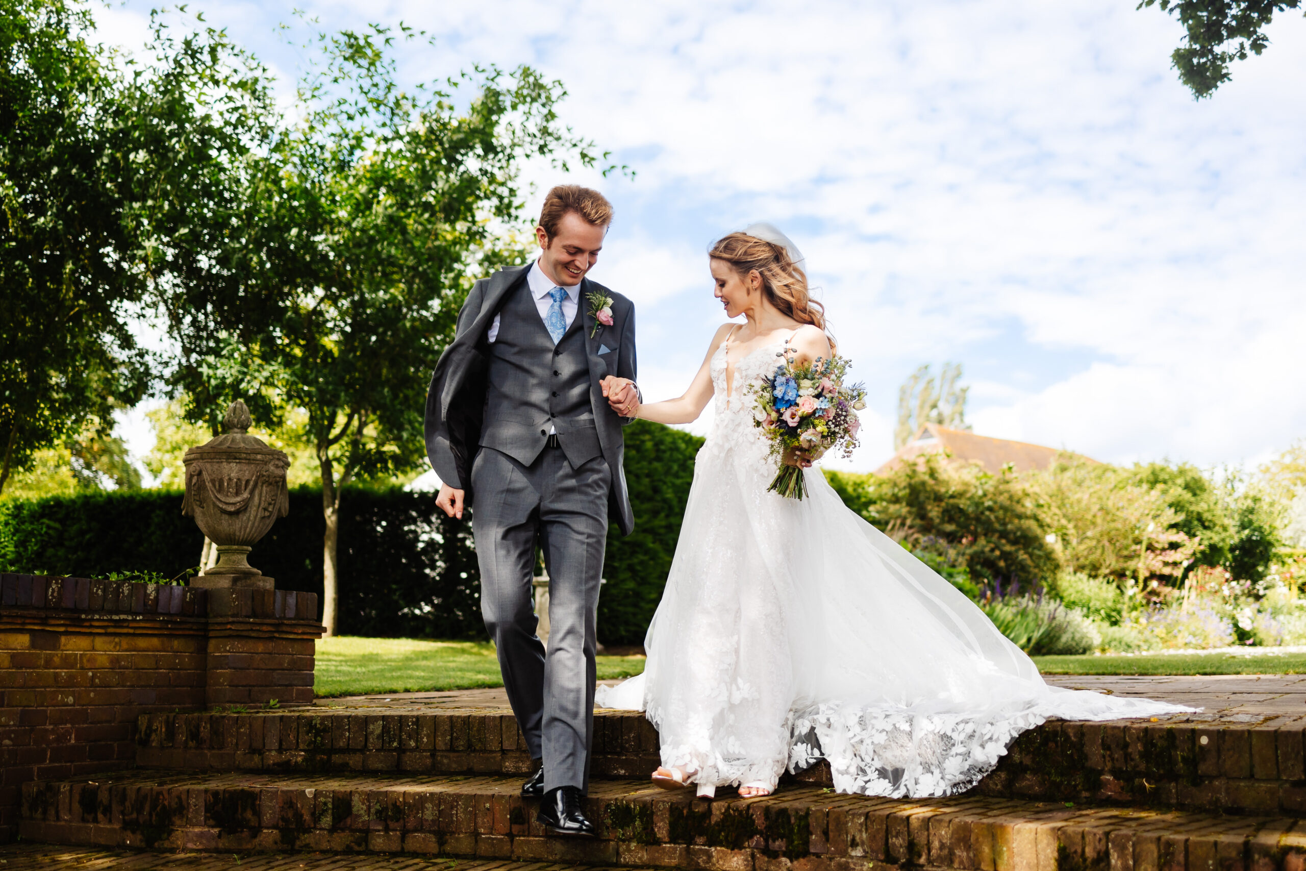 The bride and groom walking down some old steps. They are both looking down and they are holding each others hands.