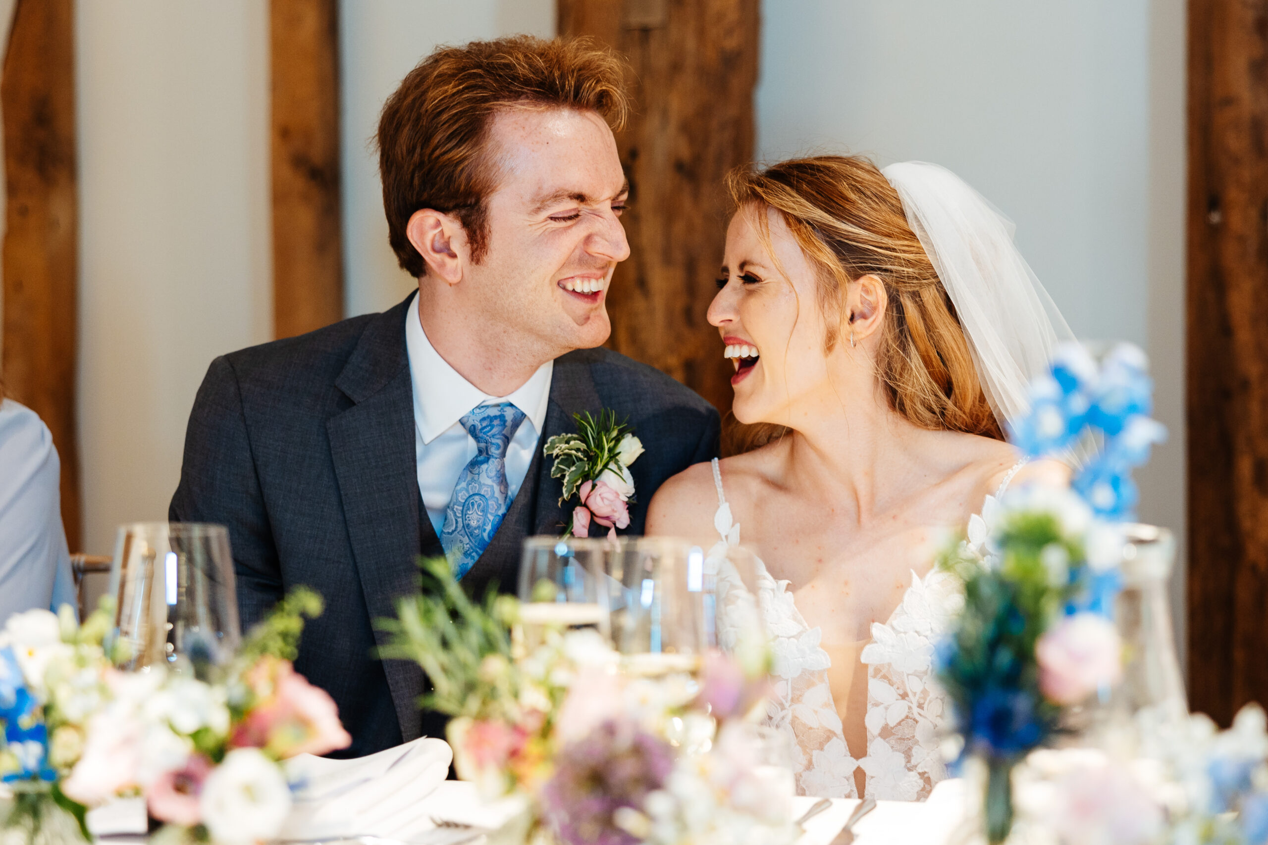 A bride and groom sat at their table. They are both laughing and smiling. 