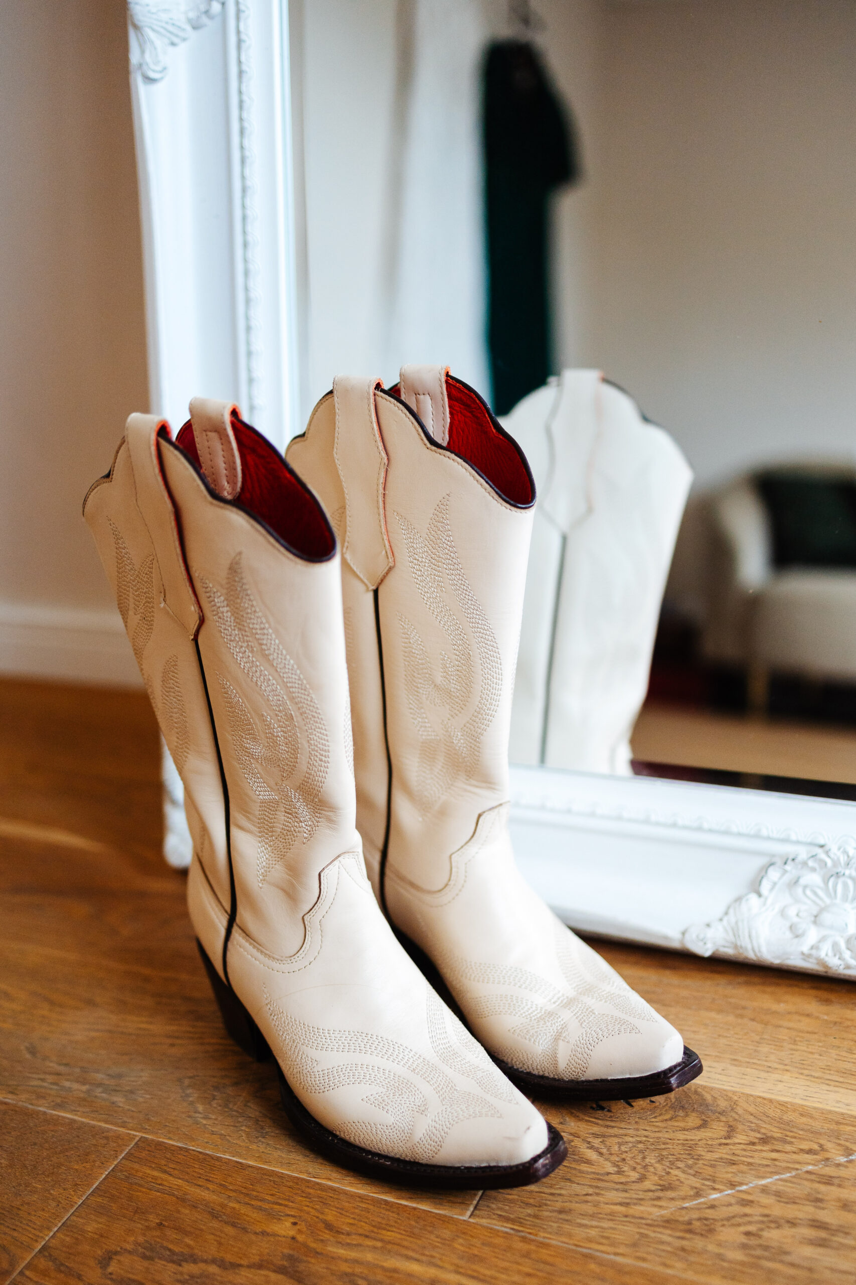 A photo of beige cowboy boots in front of a mirror. They are red inside.