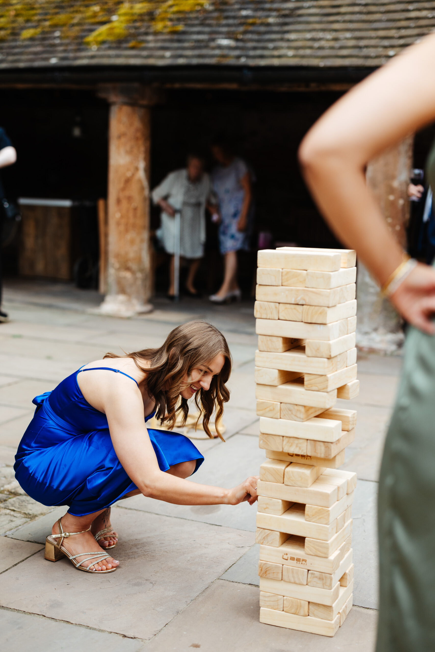 A guest in a coral blue dress playing a game of giant Jenga outside.