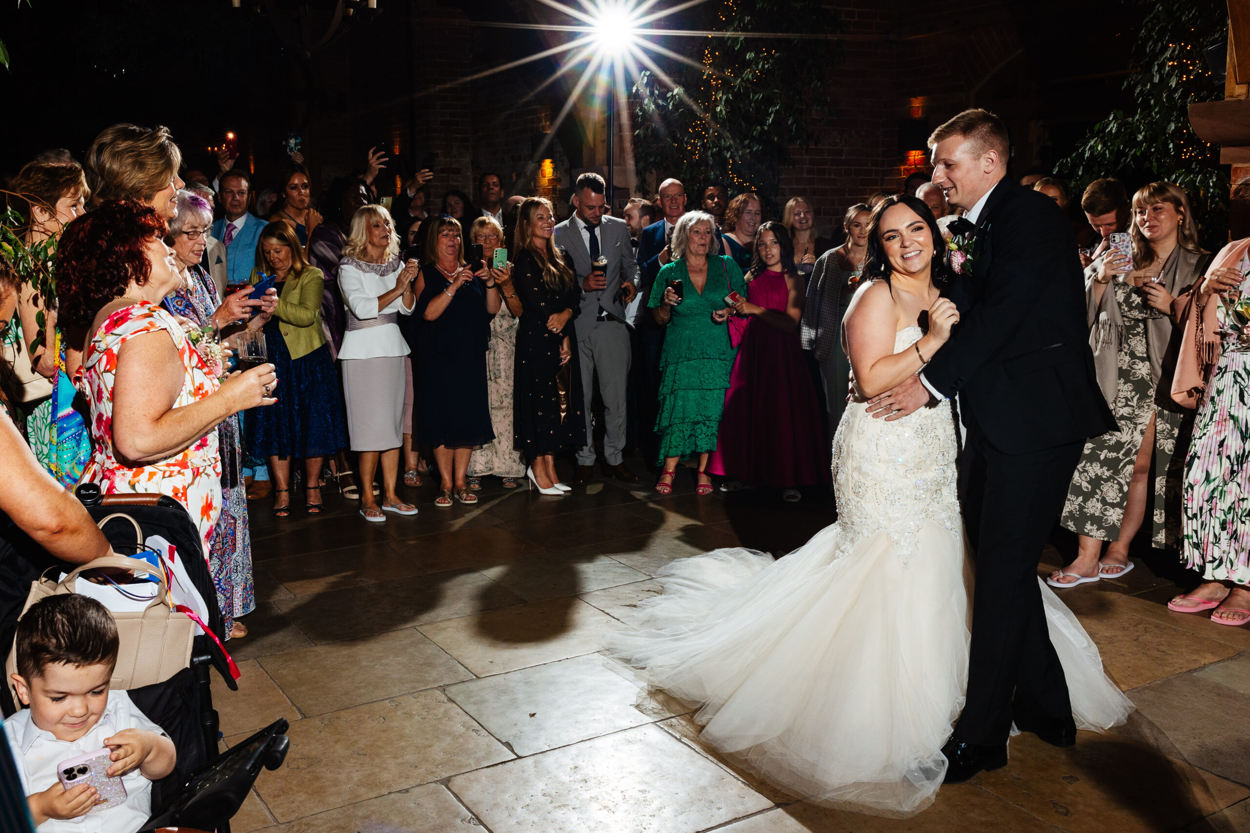 The bride and groom sharing their first dance. They are smiling and they are surrounded by their friends and family.