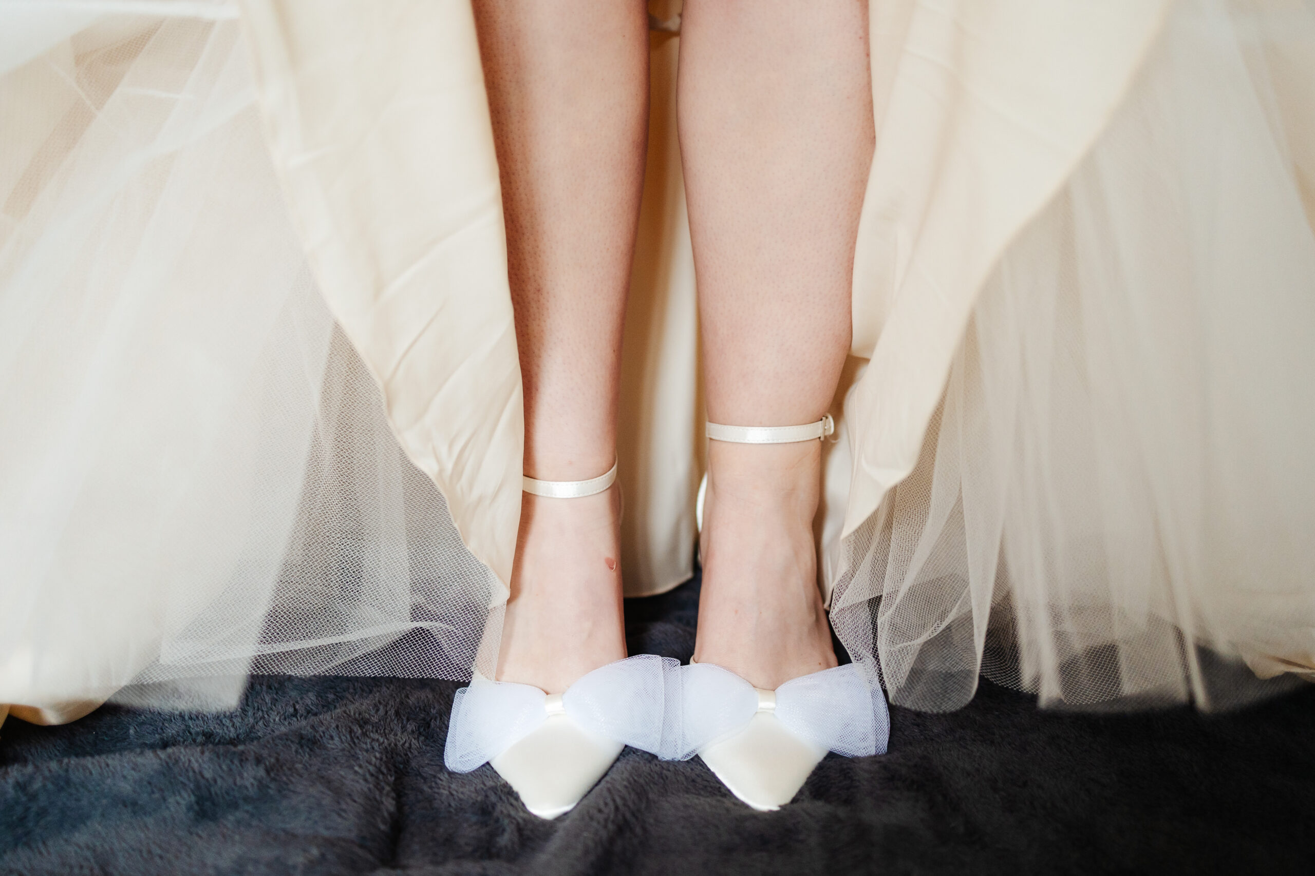 The bride's legs and feet. She is wearing white shoes with a bow on the front.