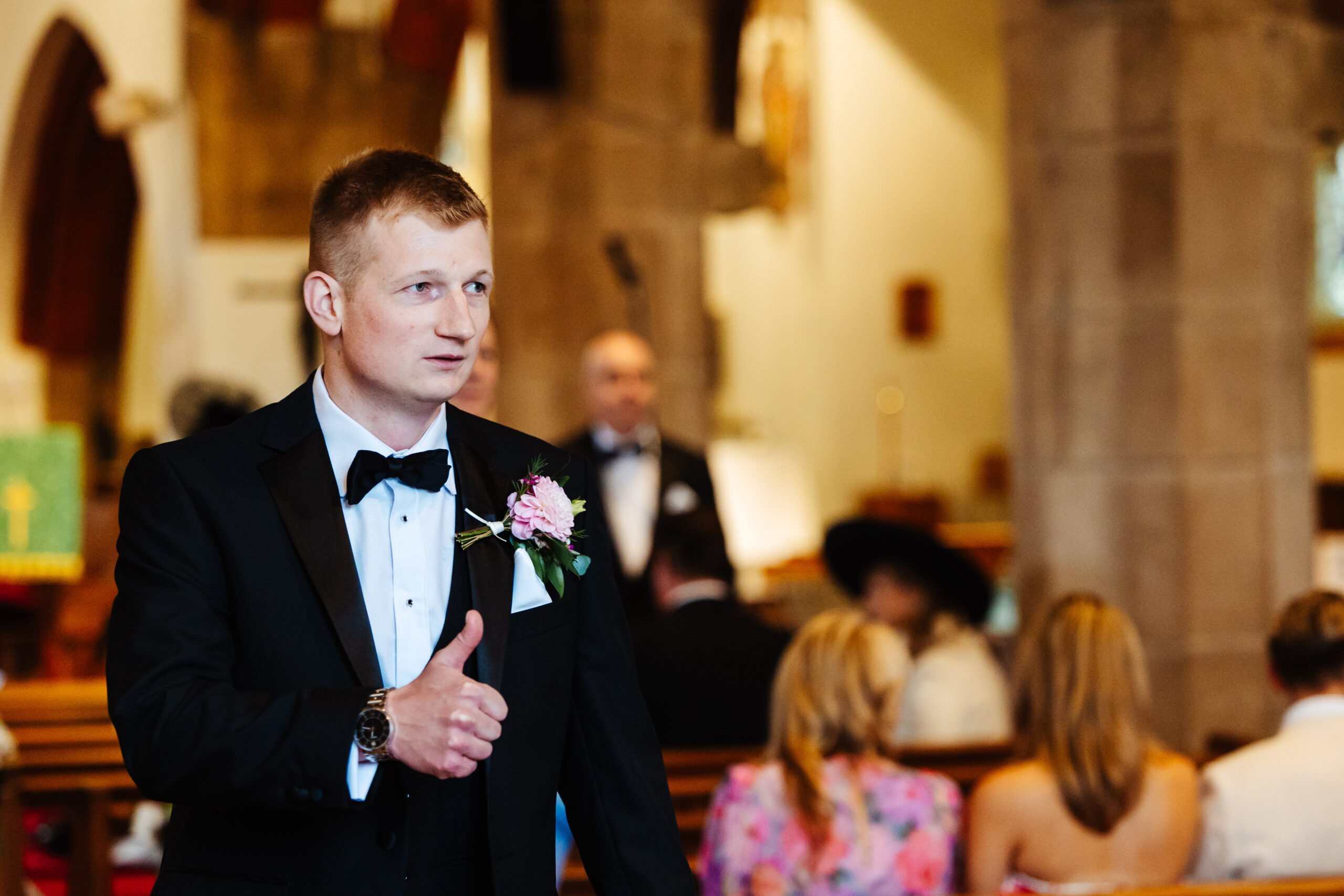 The groom in the church giving someone a thumbs up. He looks nervous.