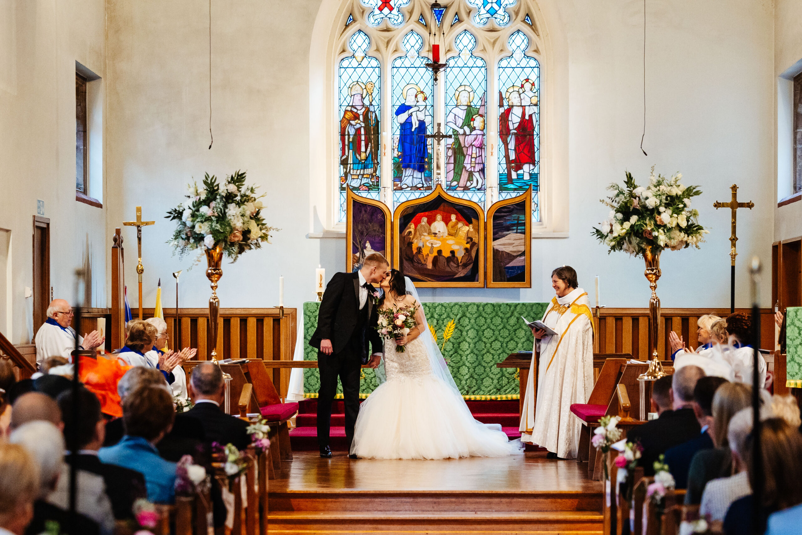 The bride and groom in the church they are kissing and they are surrounded by their loved ones.