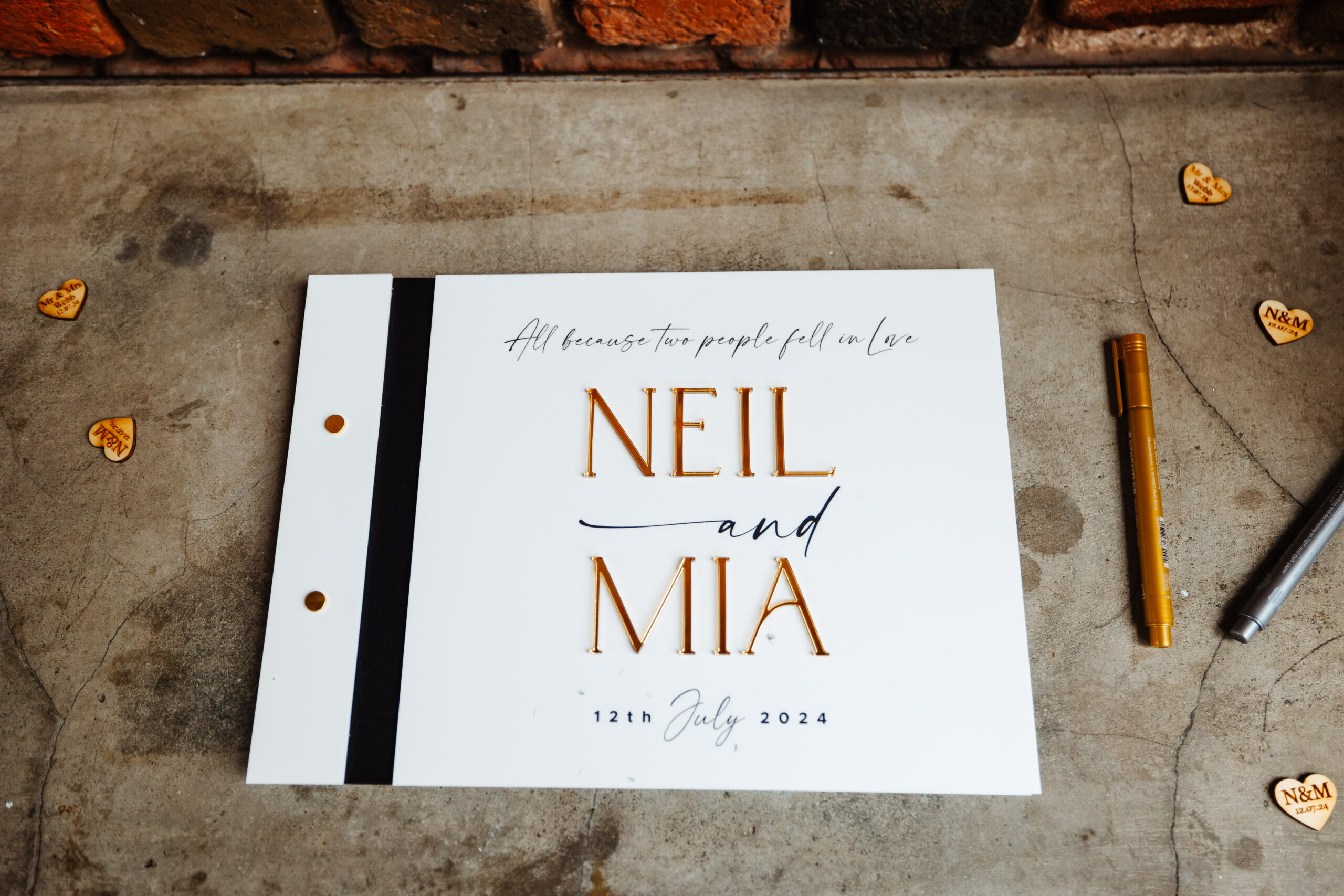 A guestbook with the following words written on it:
"All because two people fell in love
Neil and Mia
12th July 2024"