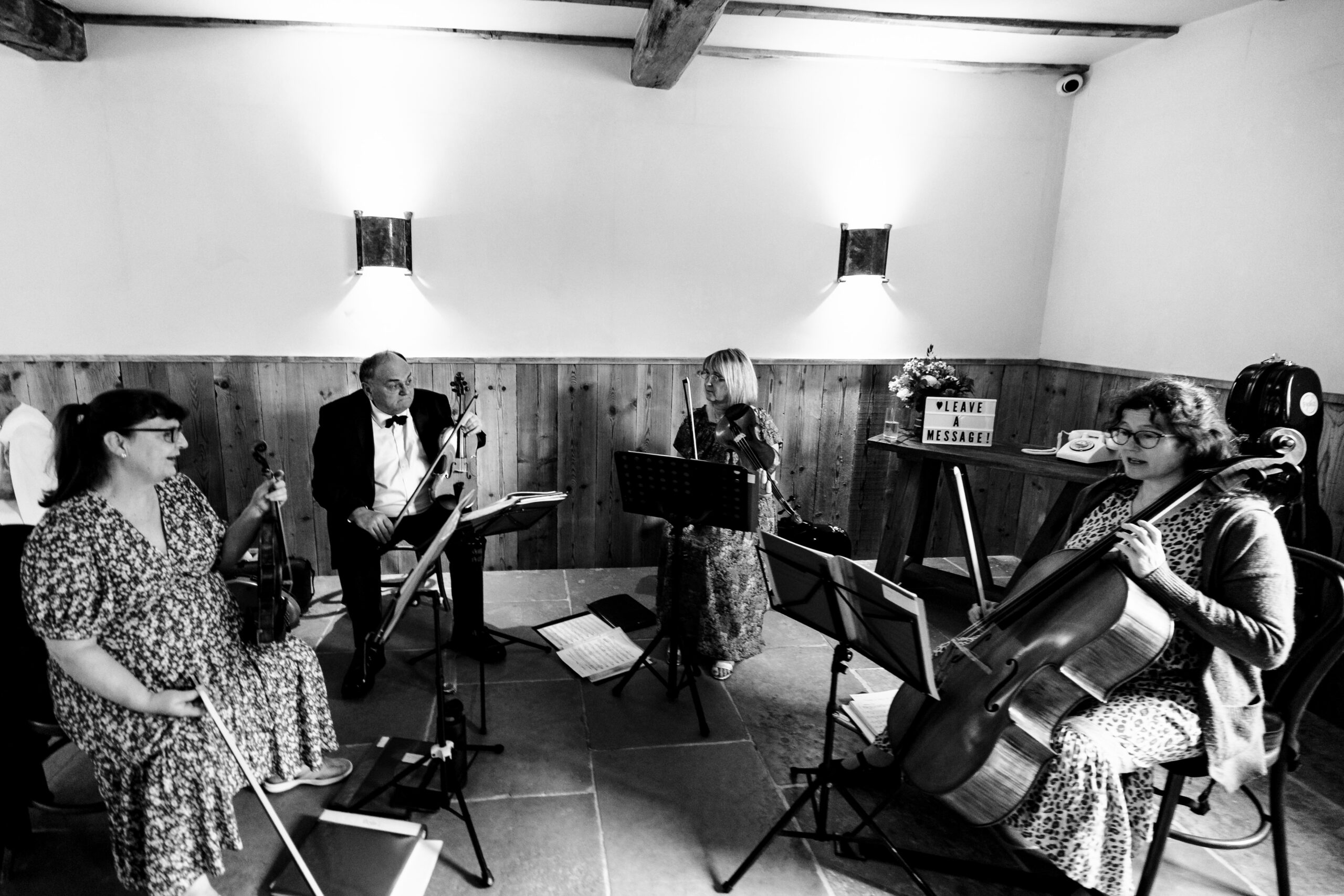 A black and white image of a string quartet playing their instruments indoors.