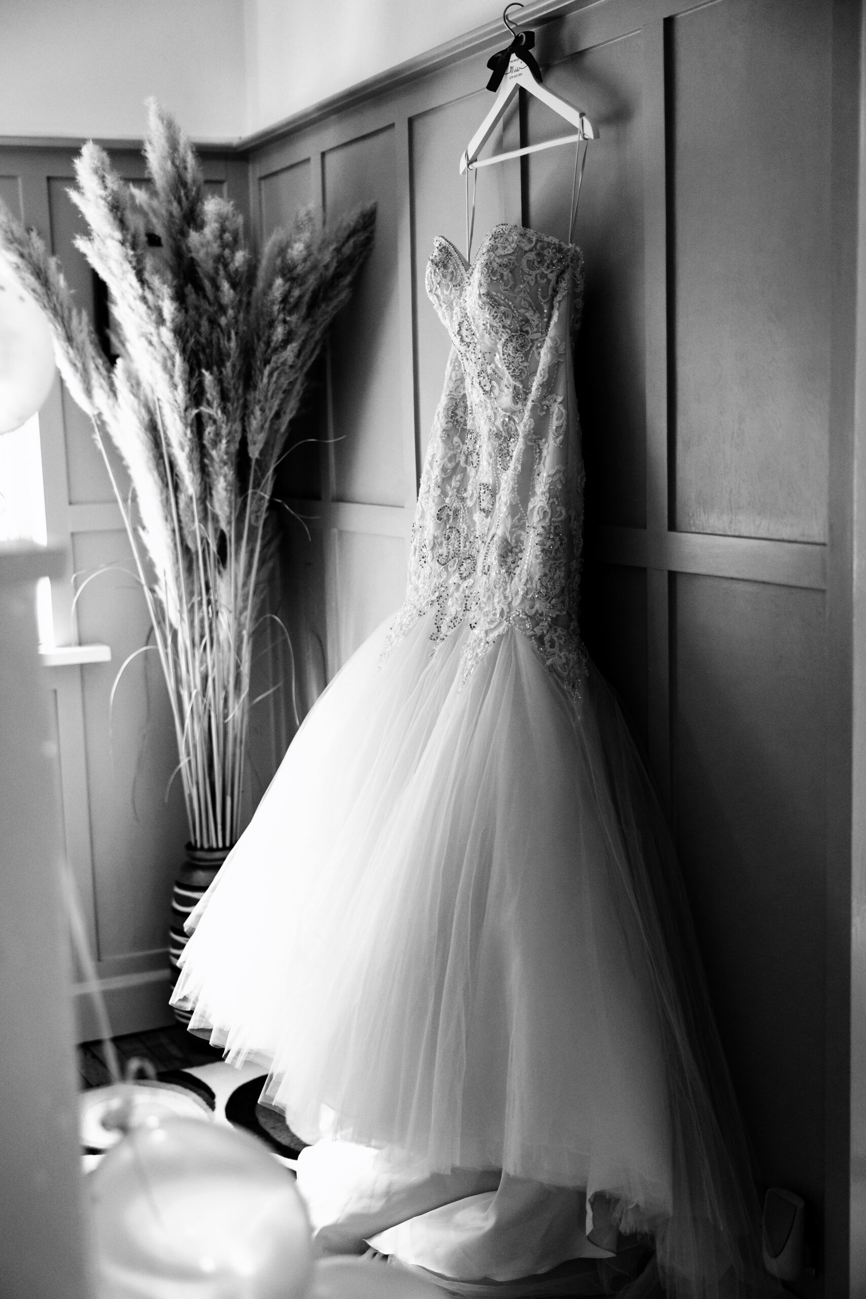 A black and white image of the bride's dress. It is beaded and laced on the front and has thin straps.