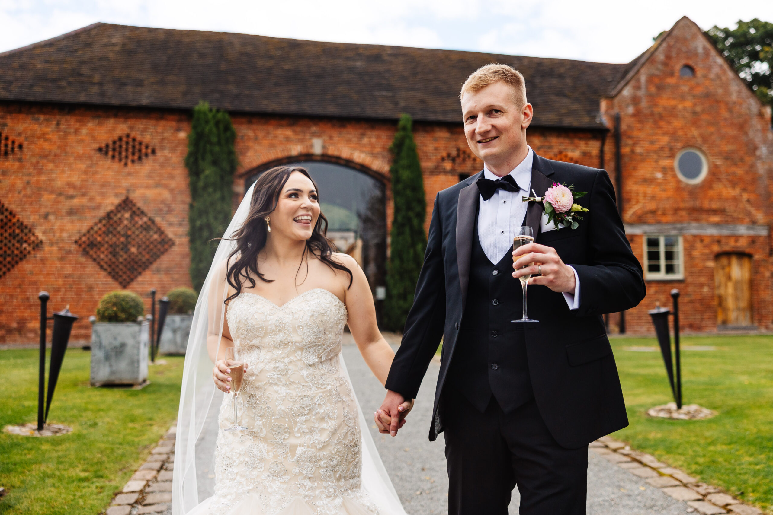 The bride and groom just after they have got married. They are holding a glass of champagne. The bride is looking at her groom and they are both smiling.