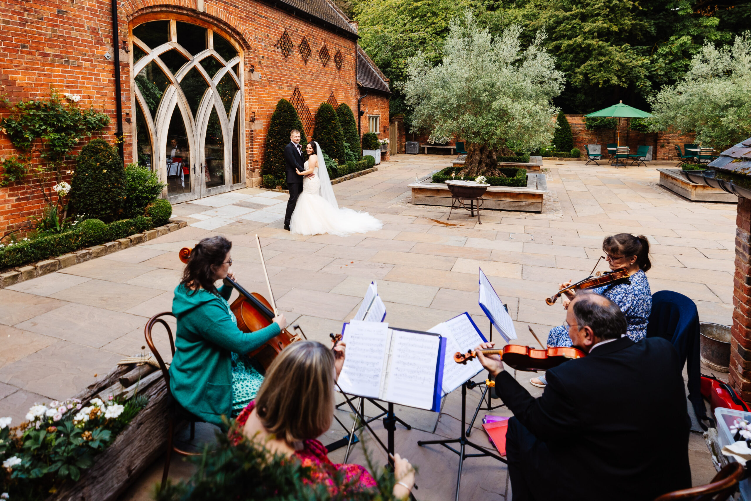 A string quartet playing their instruments outside. The bride and groom are near and are having a dance.