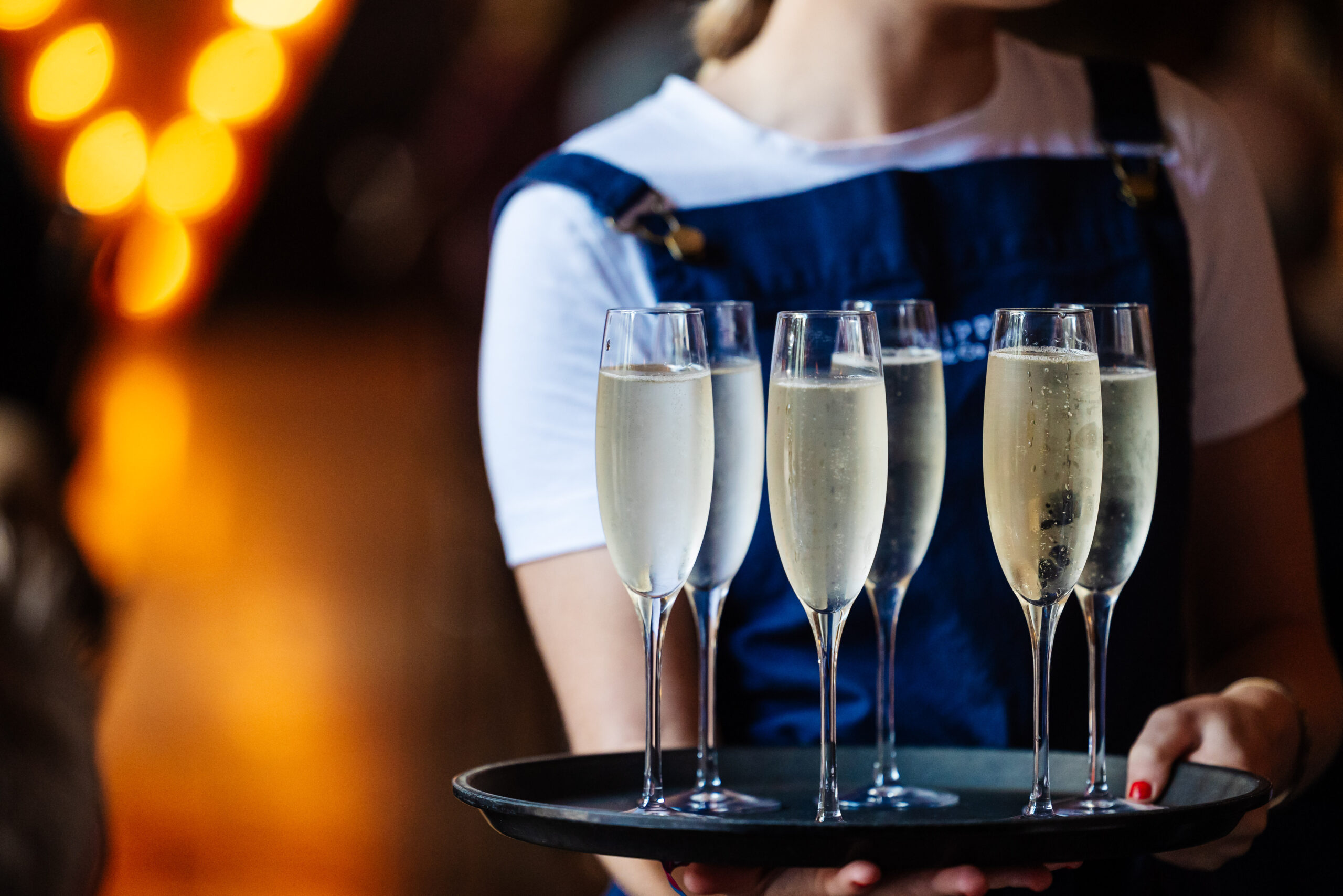 A waitress holding six glasses of champagne on a tray.