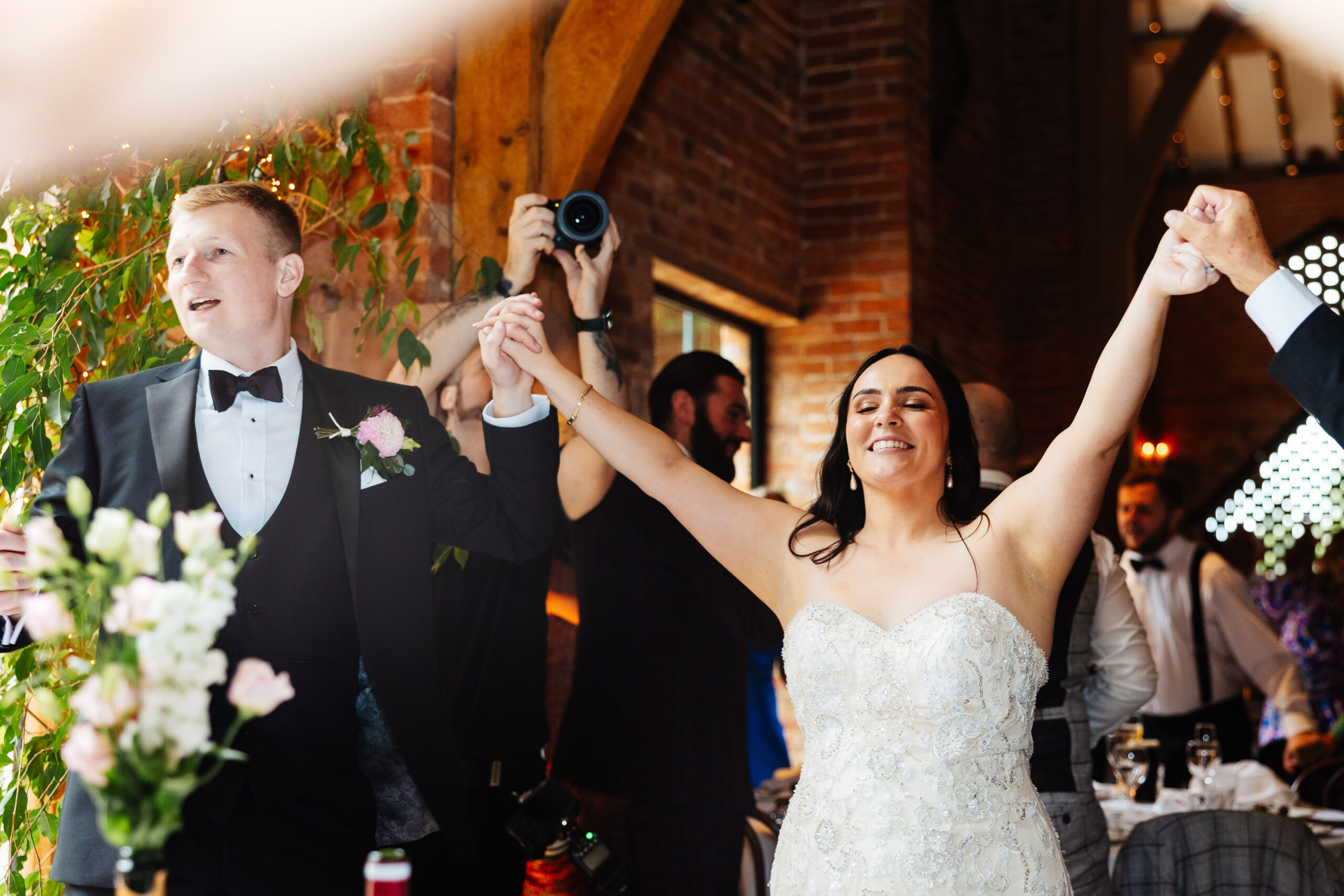 The bride and groom singing and dancing. They are holding hands and have their hands in the air having lots of fun.