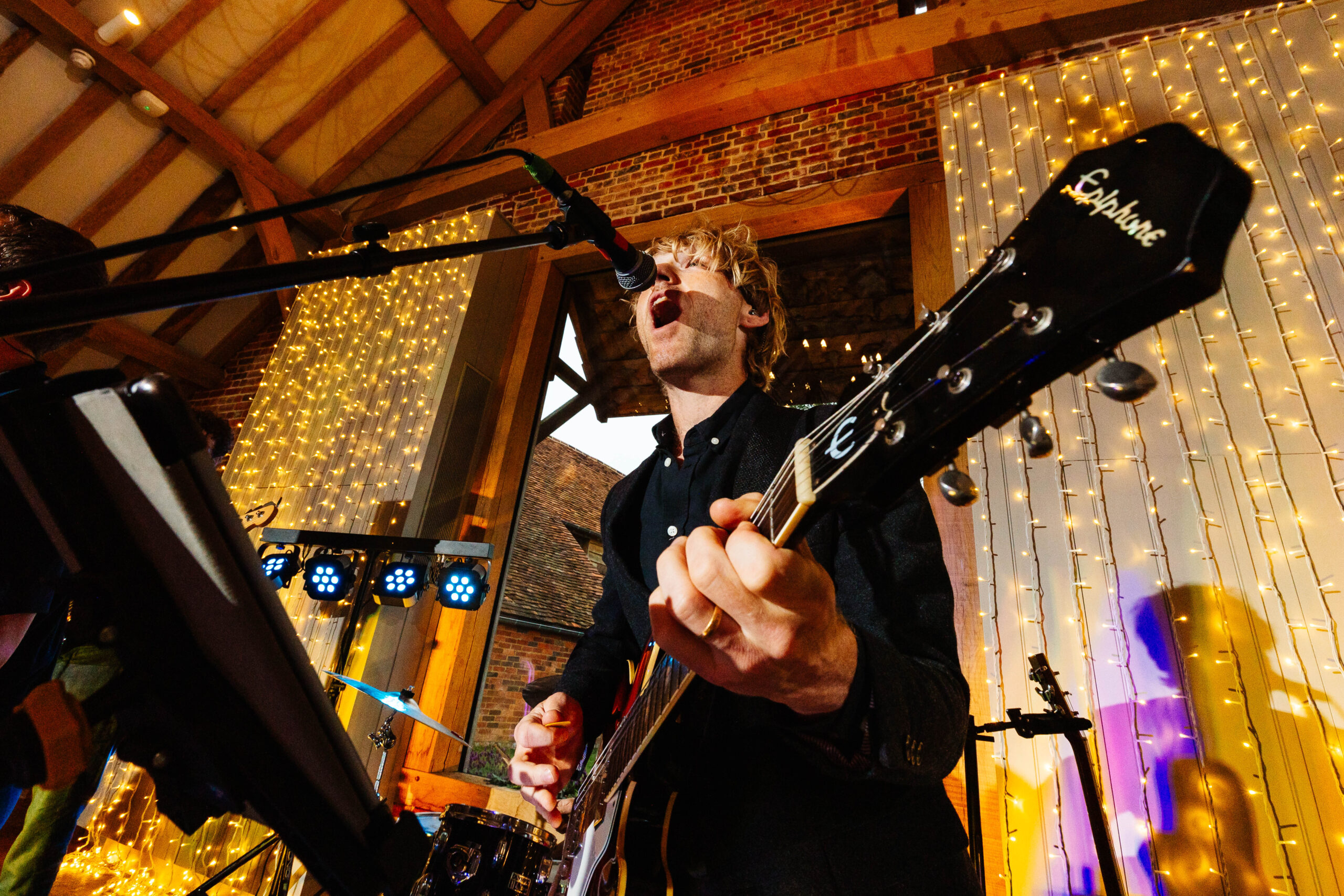 A photo of a musician. He is playing guitar and is singing in to a microphone.