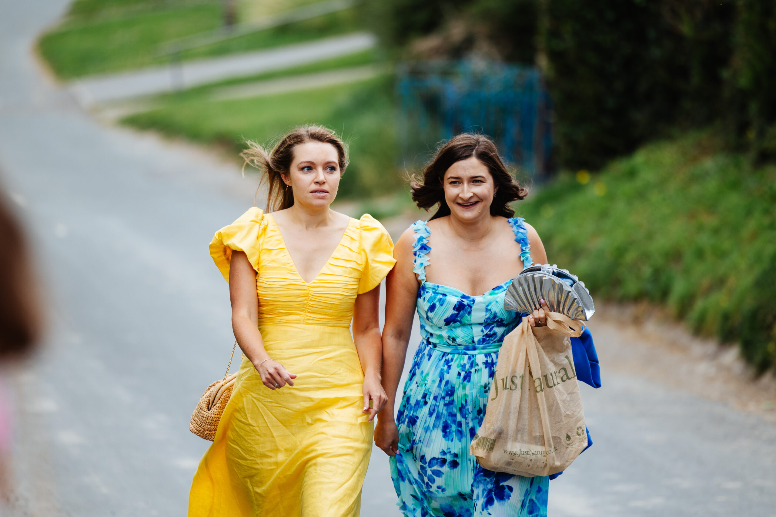 Guests are arriving. Two ladies, one wearing a yellow dress with large shoulder pads and the other in a blue strappy dress.