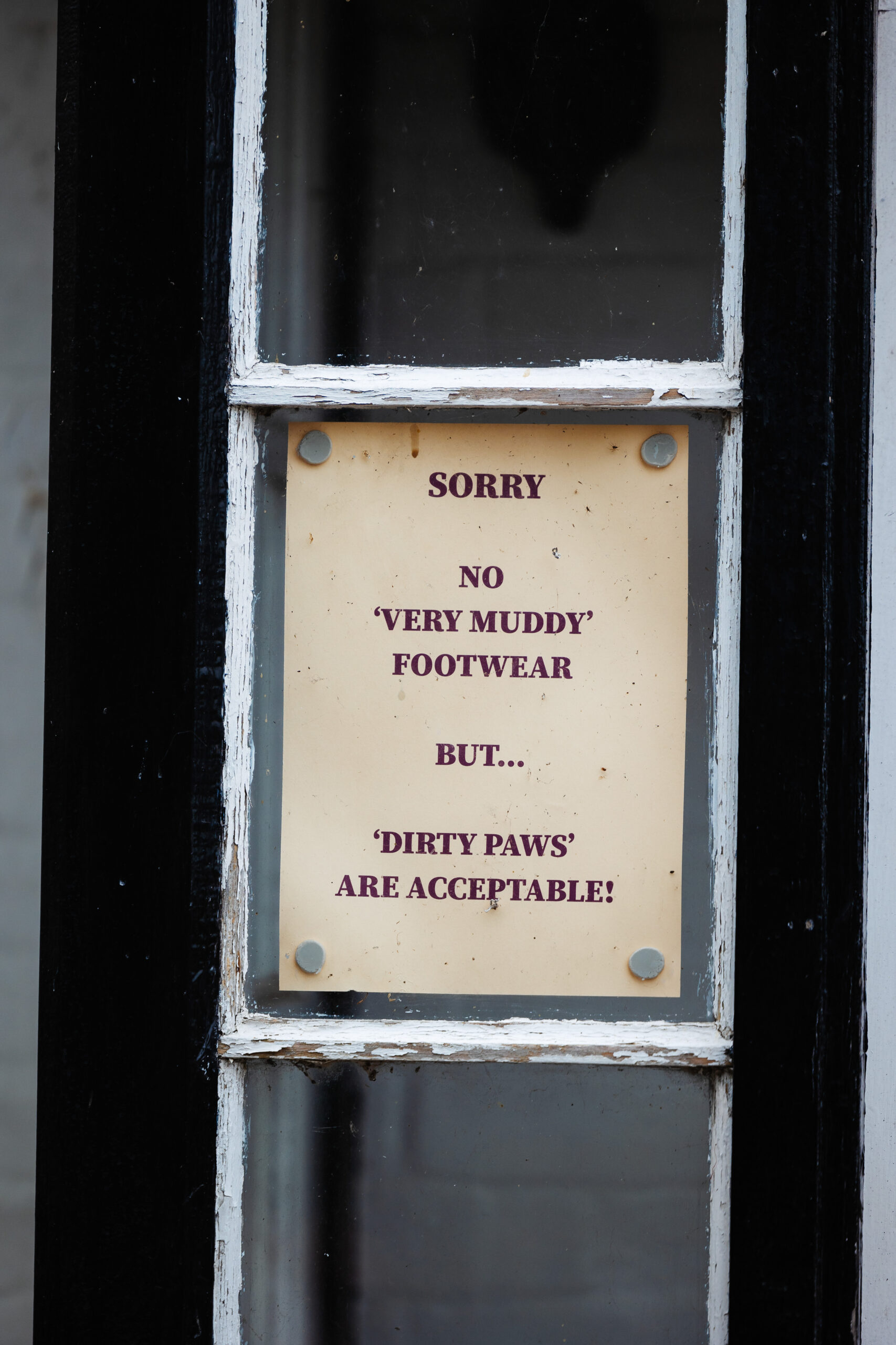 A sign on a pub door saying "Sorry, no very muddy footwear, but dirty paws are acceptable'