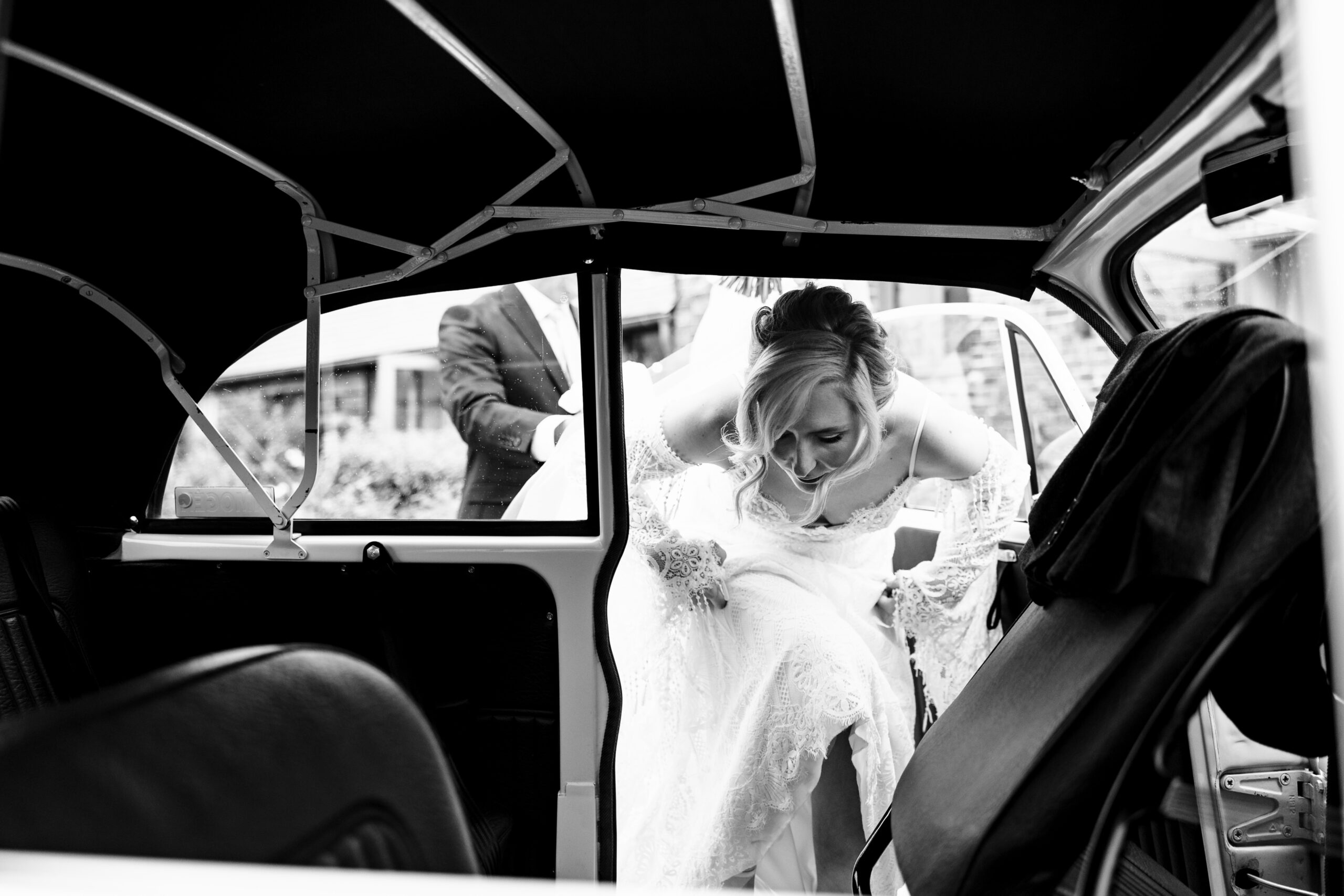 A black and white image of the bride getting in to the wedding car.