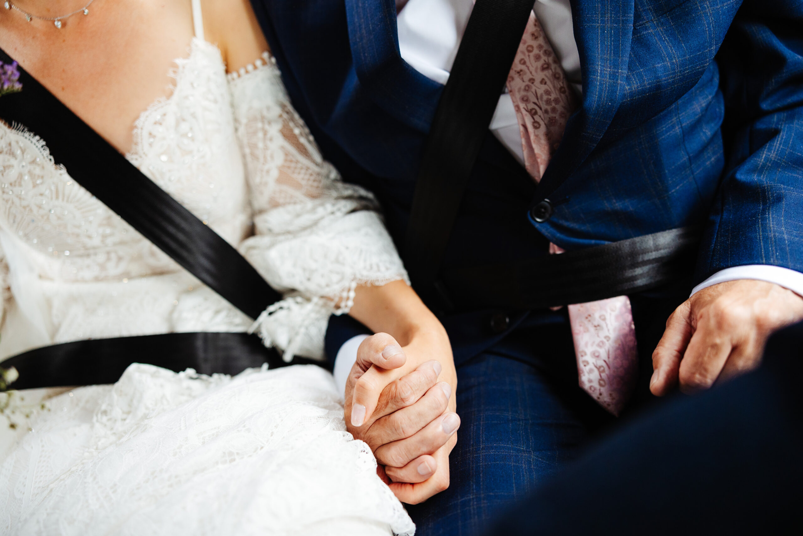 A photo of the bride and her father in the car on the way to her wedding. They are holding hands.