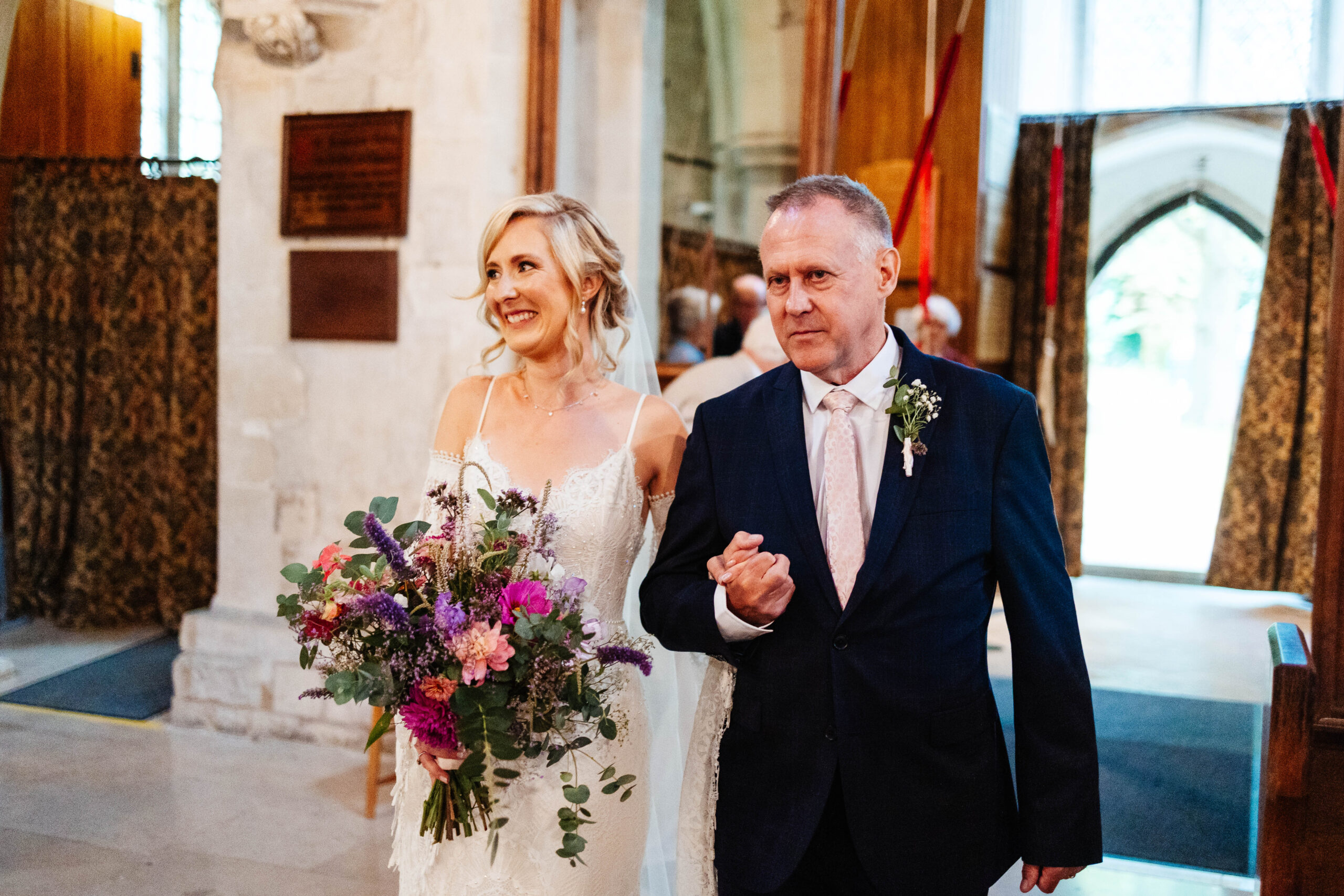 The bride and her father walking down the aisle. The bride is smiling.