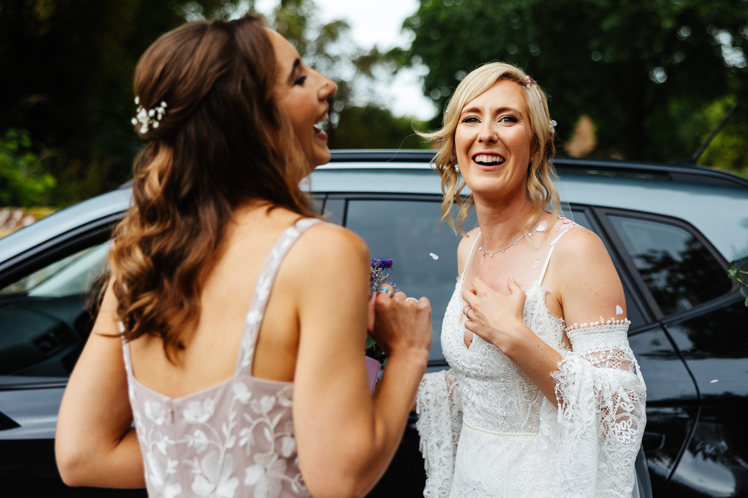 The bride and a bridesmaid. The bride is looking at the camera and smiling and the bridesmaid is looking away from the camera and smiling.