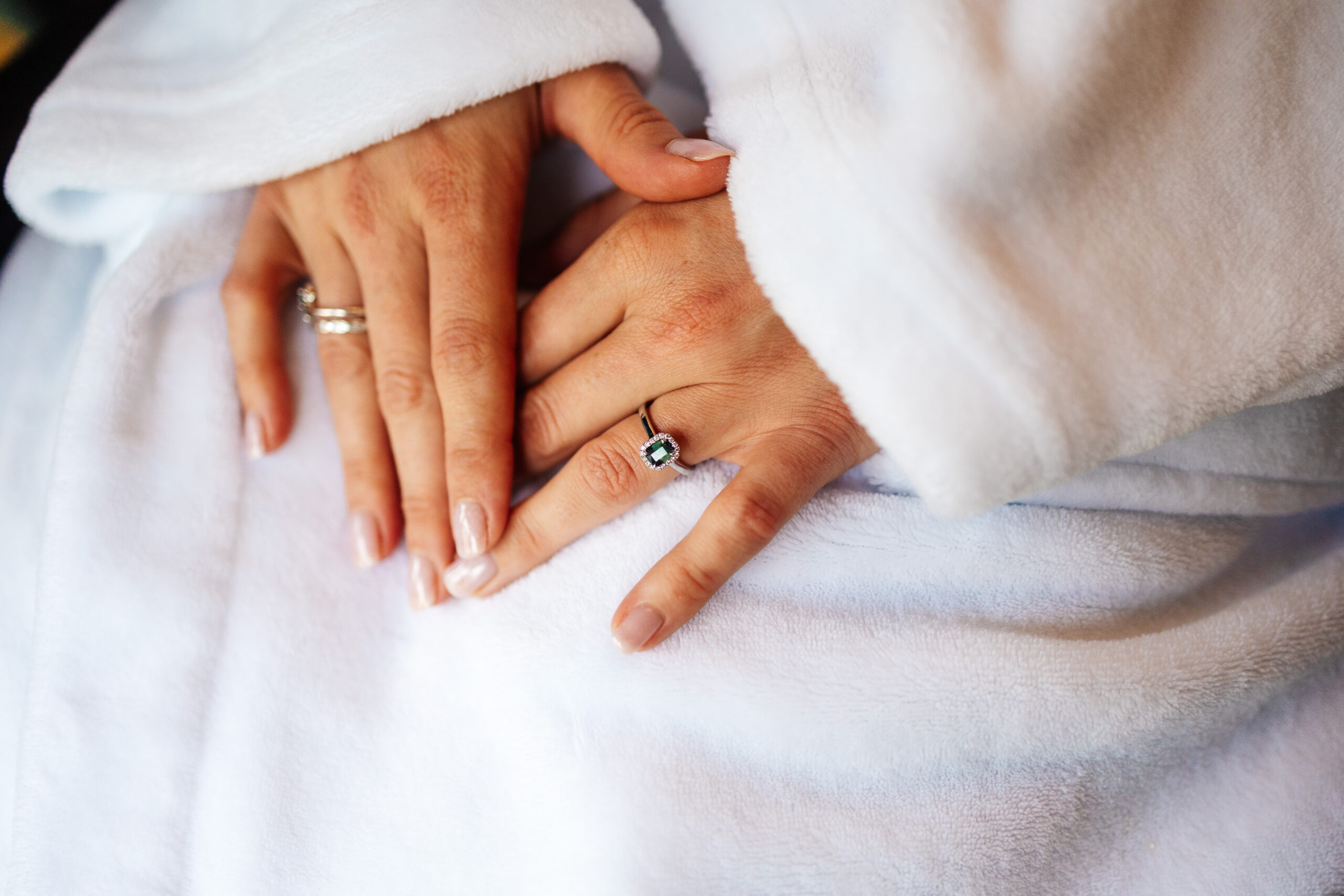 The brides hands. She has them on top of her white dressing gown and she has her nails painted in a pale pink colour. You can see her engagement ring clearly.