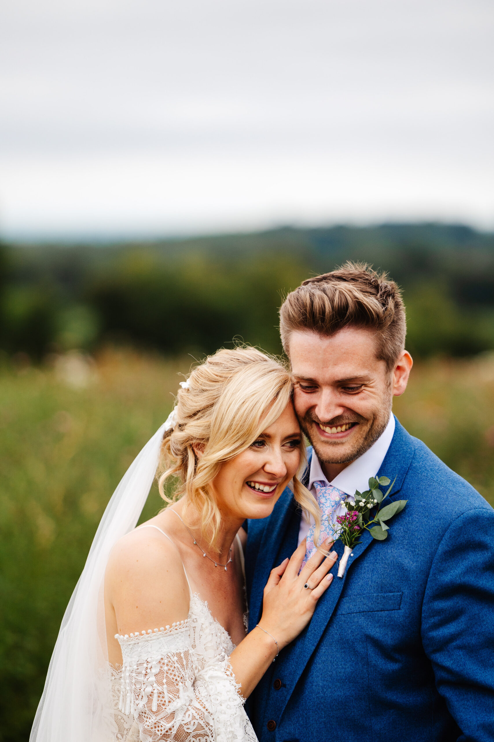 A close up image of the bride and groom. The bride has her hand on the groom's chest. They are both smiling.