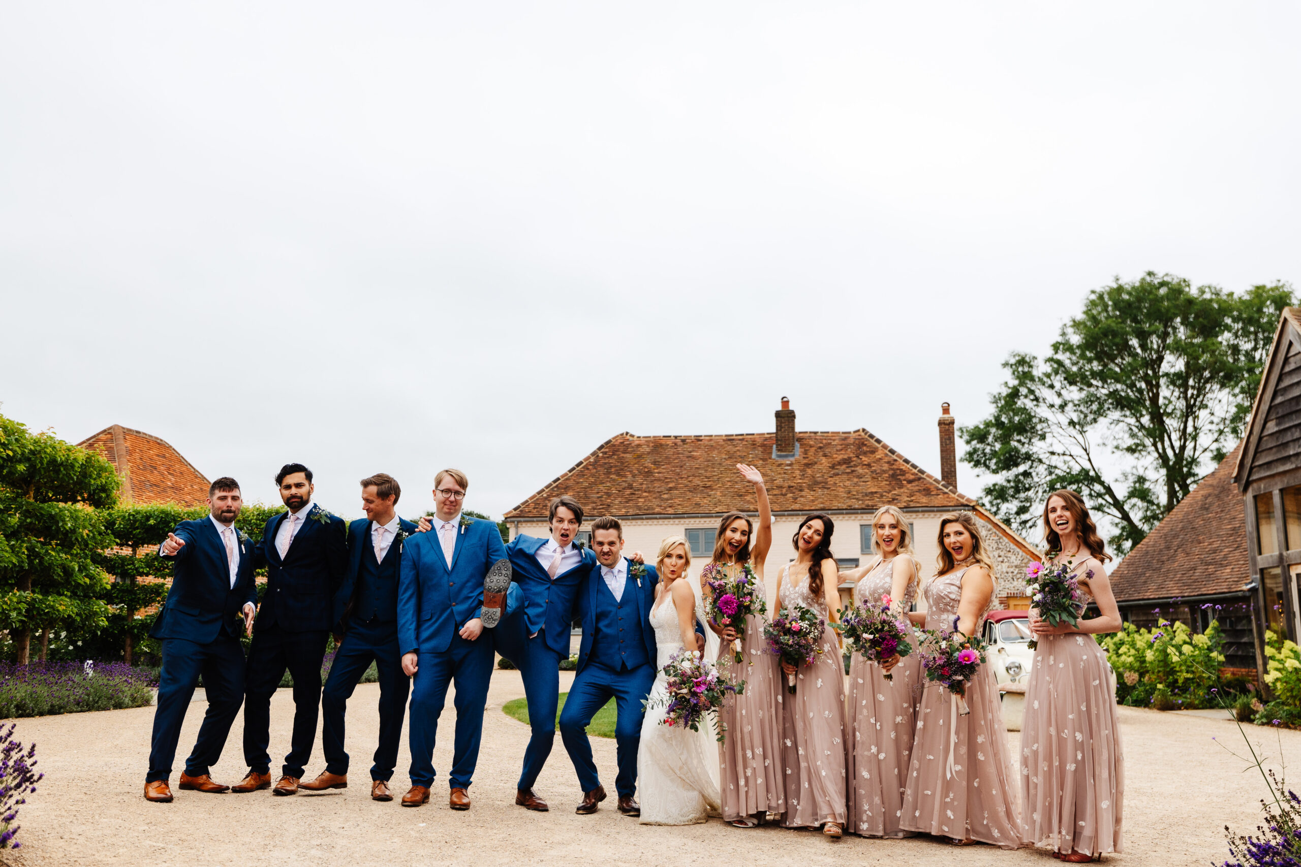 A photo of the bridal party; both groomsman and bridesmaids. The bride and groom are in the middle. They are having a good time and have their hands in the air.