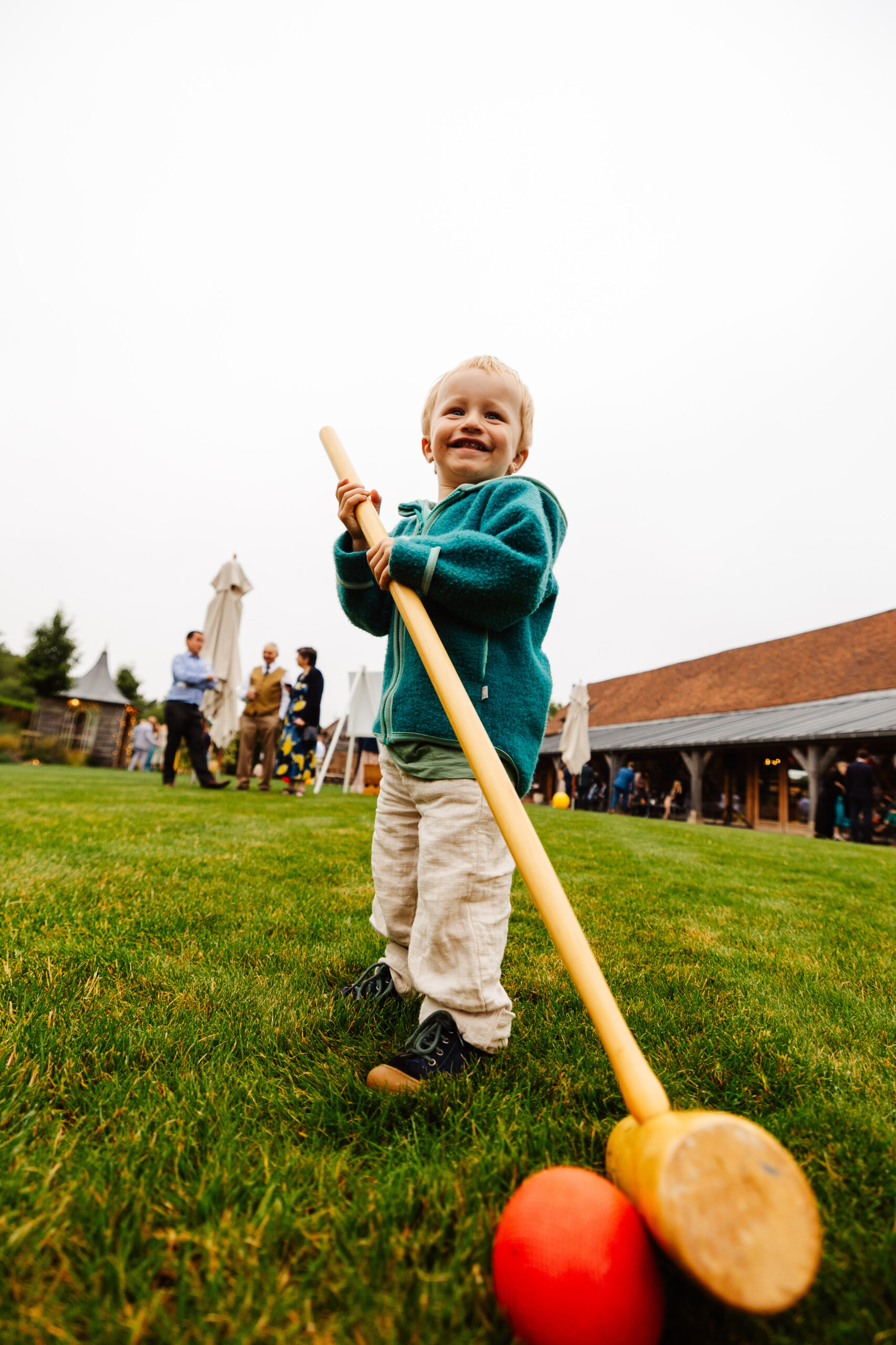 A little boy holding a croquet stick. He is hitting the ball and looks like he is having a fantastic time.