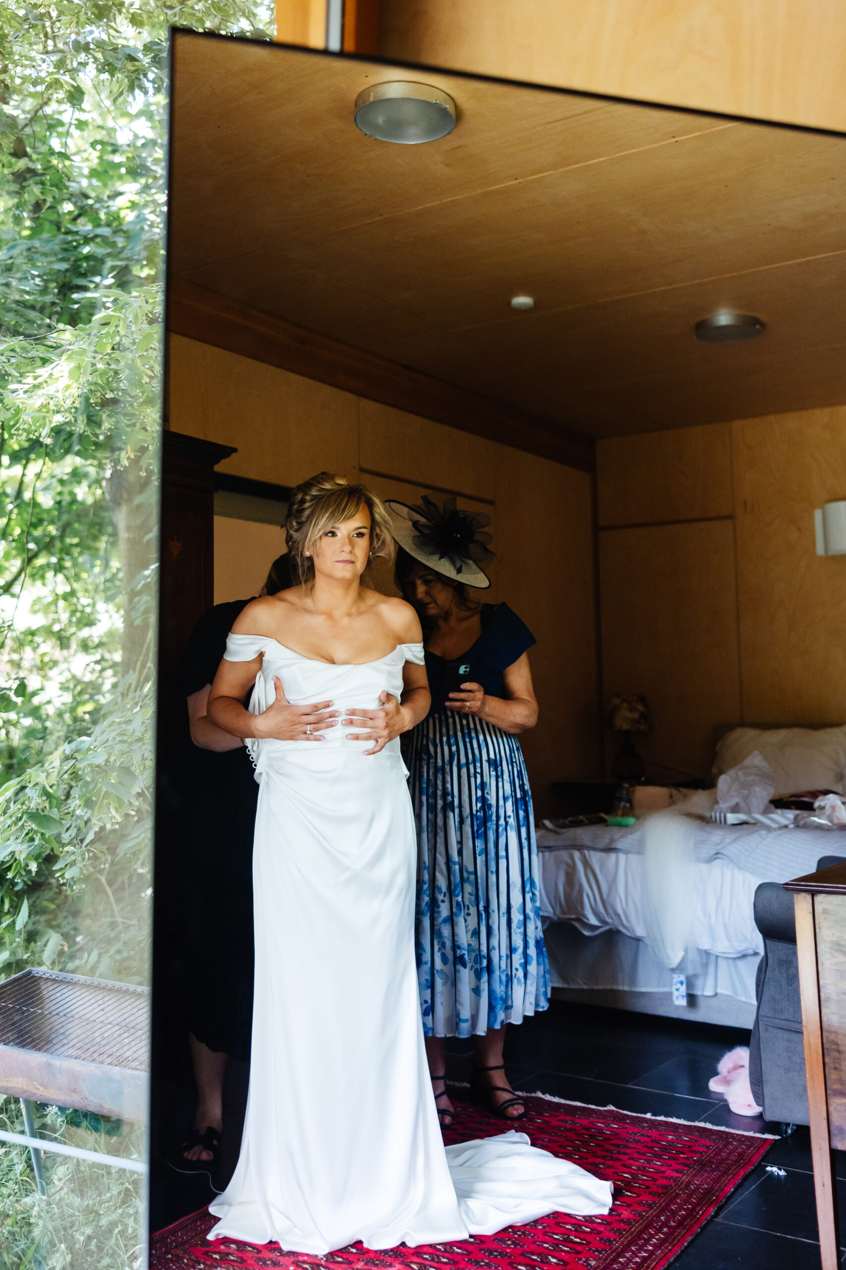 A photo of the bride getting ready in her wedding dress. Her hair is pinned up and she is holding on to her dress.