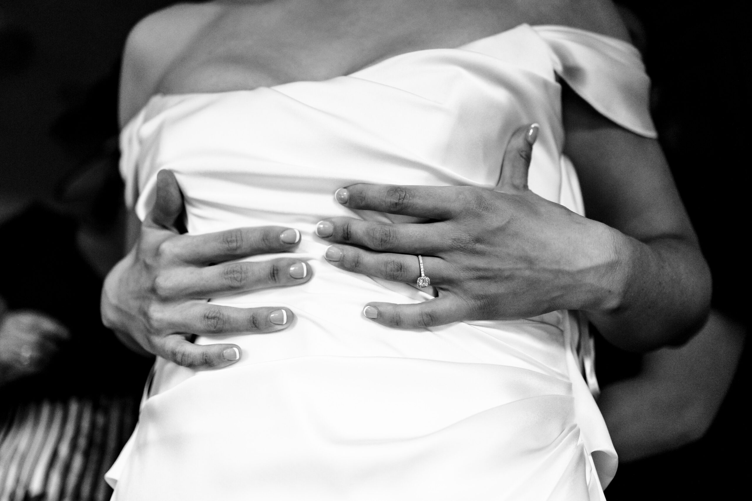 A black and white image of the bride's hands on her wedding dress. She has a french manicure and you can see her sparkly engagement ring.