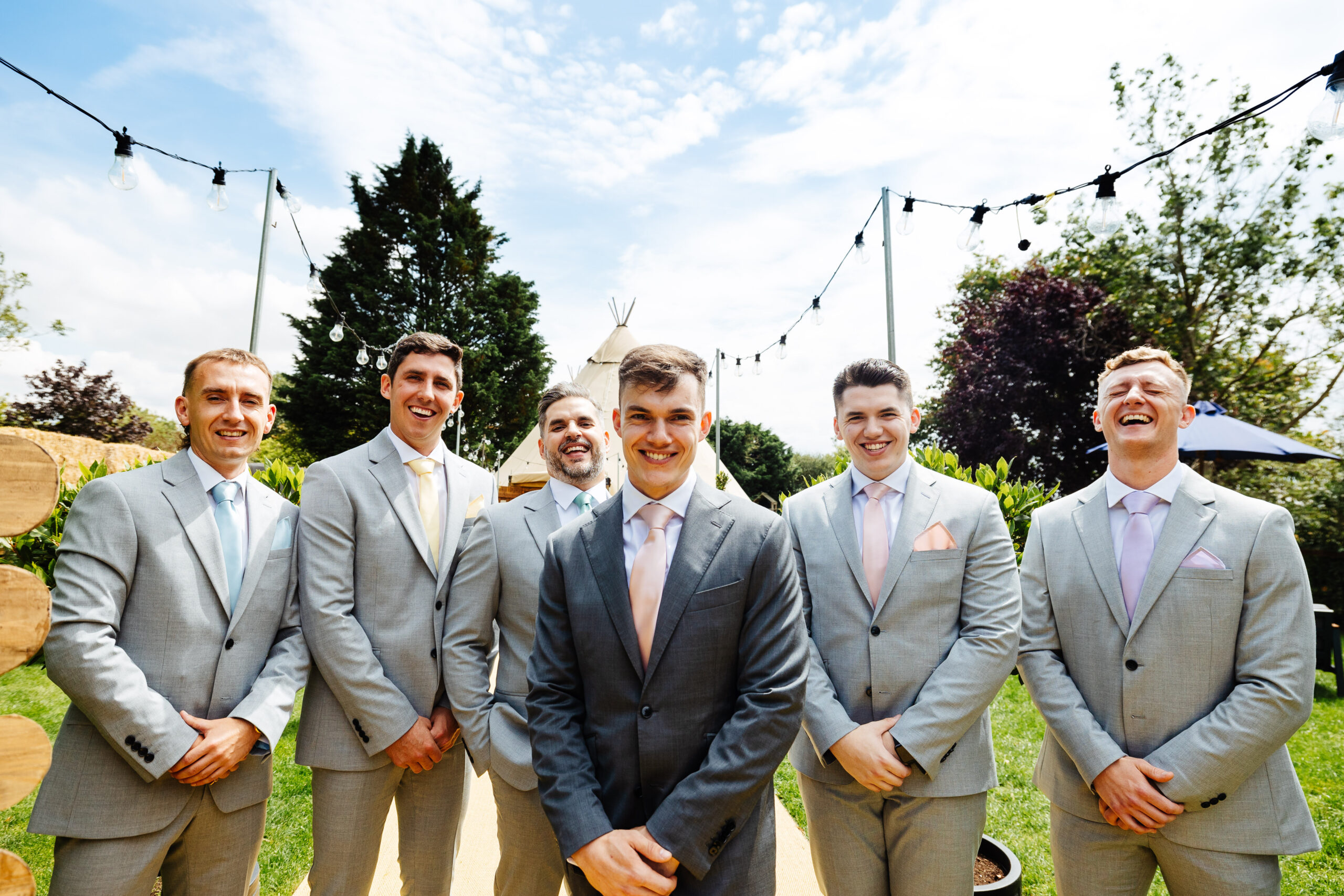 A group shot of the groom's party. They are wearing light grey suits with a pastel colour tie and James is in a darker grey suit with a pink tie.