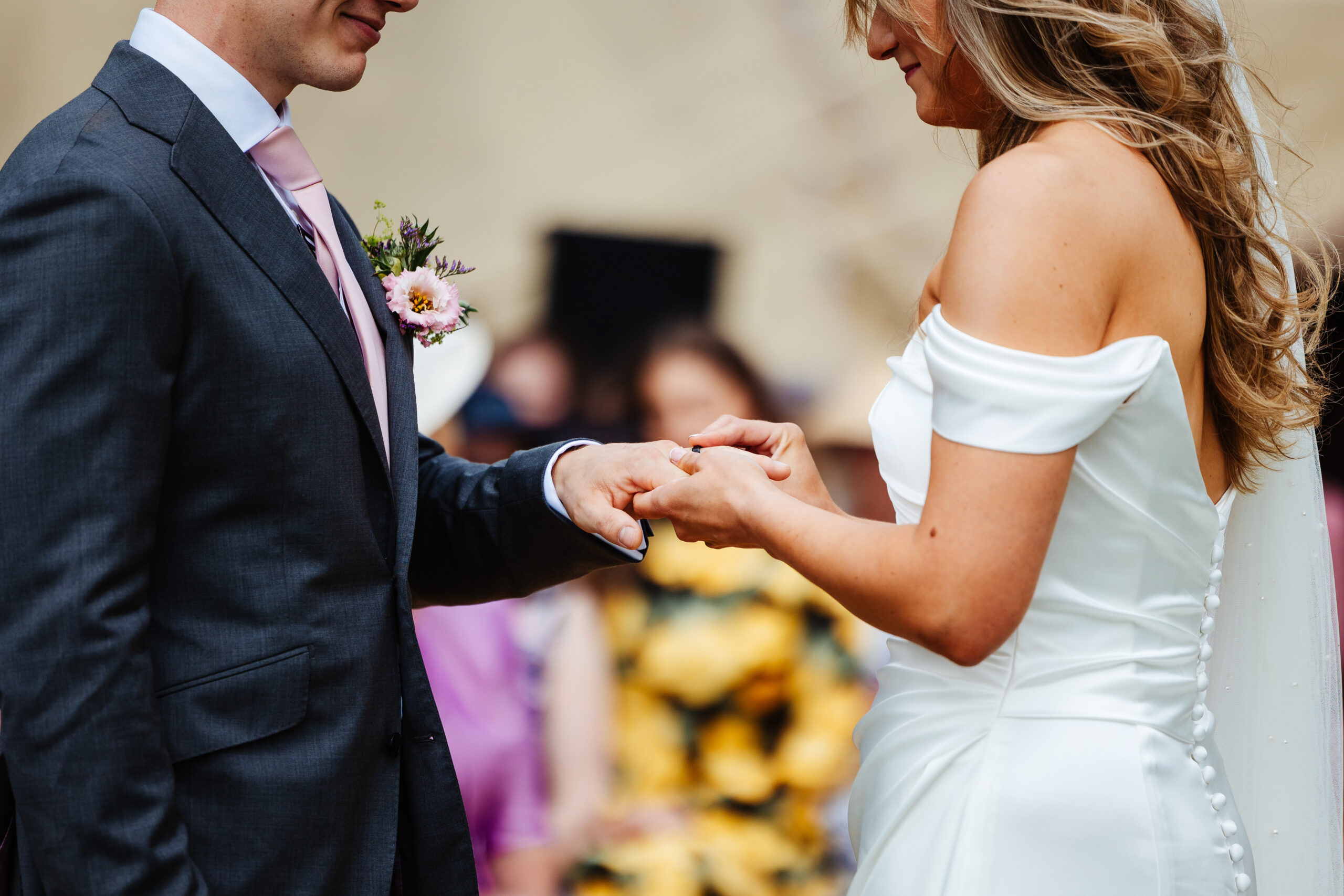 The bride and groom exhanging rings. The photo is a close up of the hands and faces of the two.