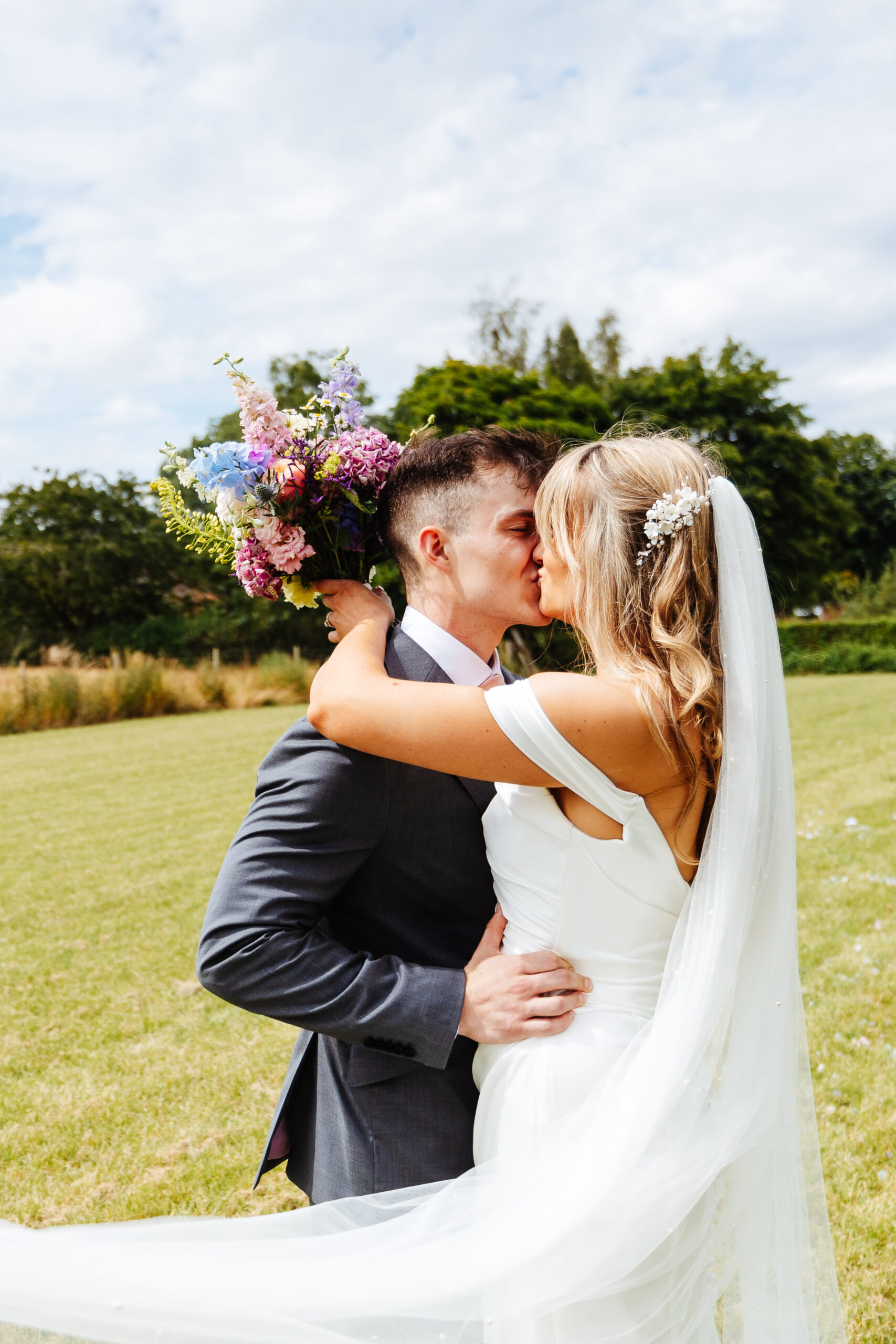 The bride and groom outdoors sharing an intimate kiss. The groom has his hands around the bride's waist.