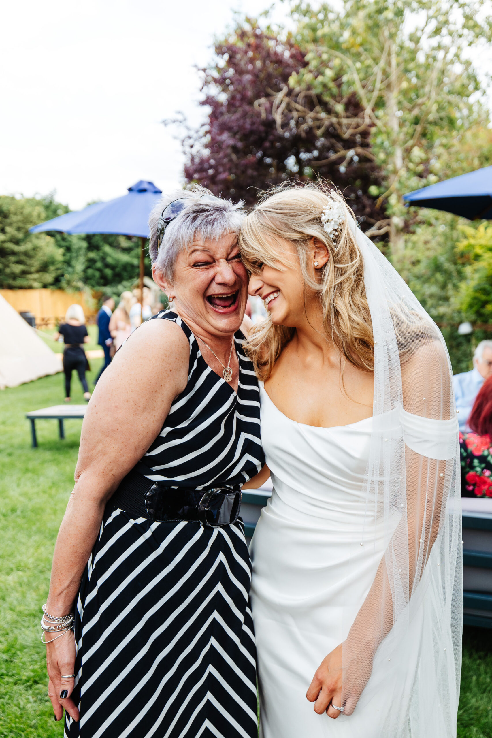 The bride and a guest laughing and smiling. They are holding one another. You can see the bride's veil has small, pearls on it.