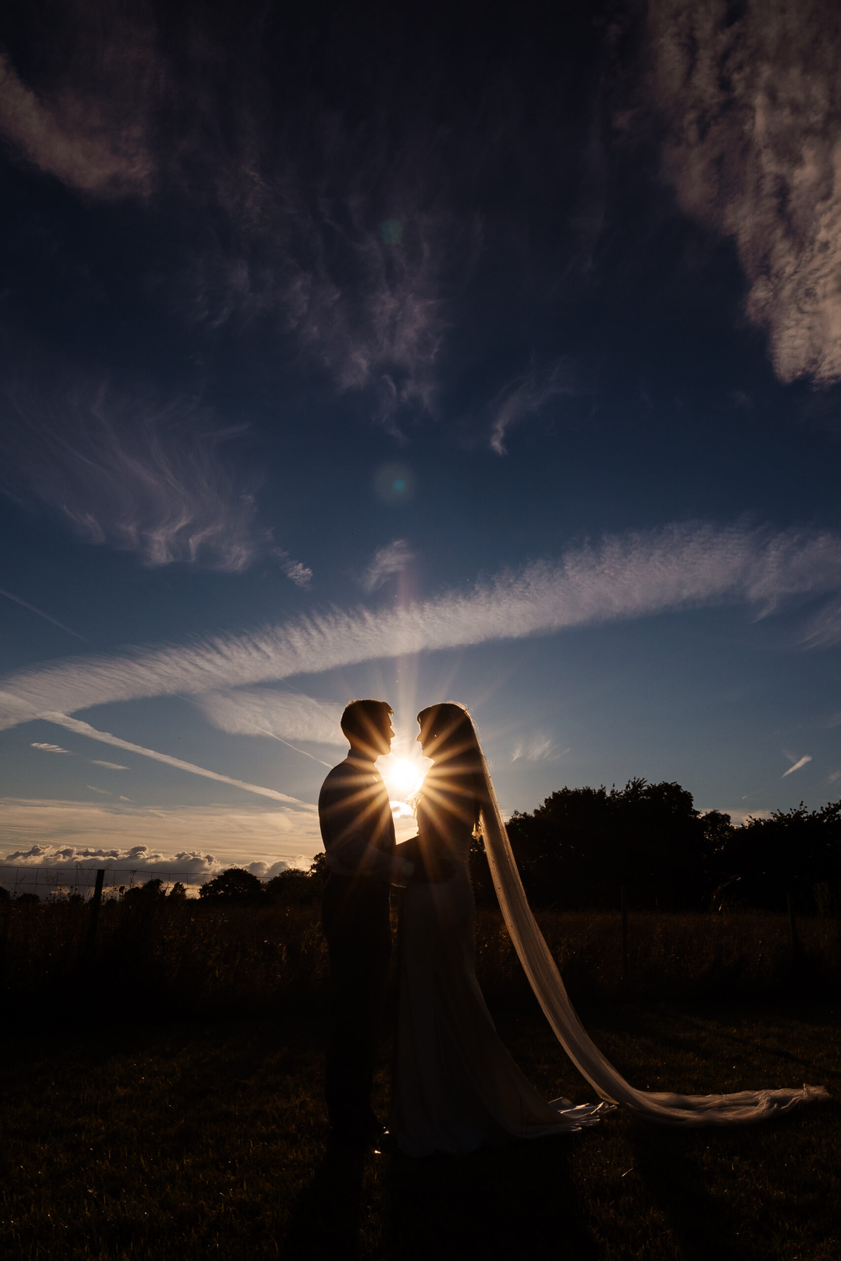 An image of silhouette of the bride and groom. There is just enough space between them where the sun that it setting, is shining through.