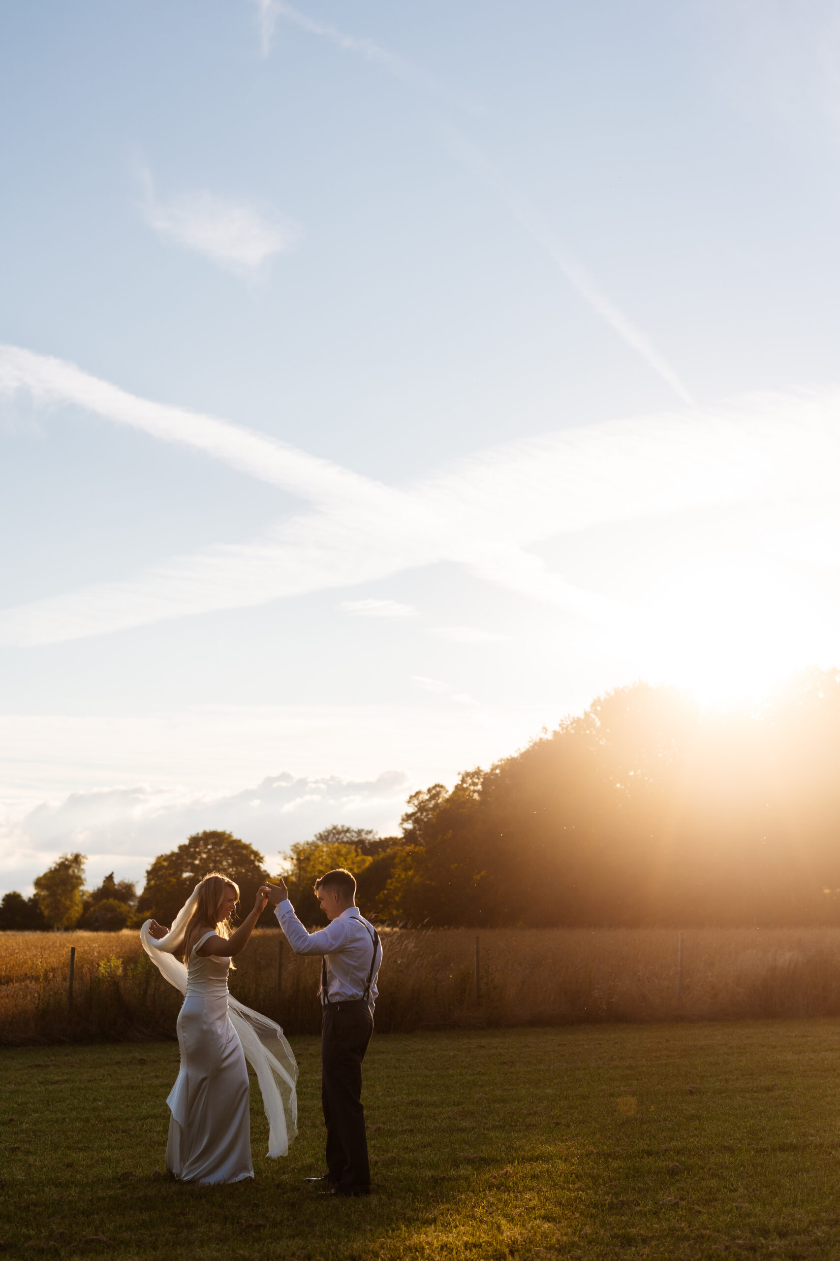 The bride and groom outside in a field dancing. The sun is setting in the background