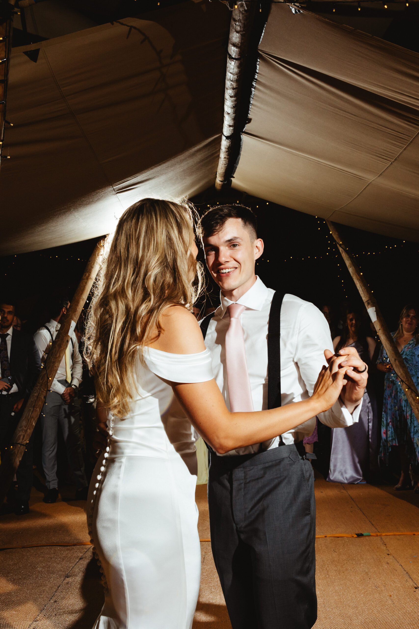 The bride and groom sharing a first dance. The groom is looking at the camera and smiling.