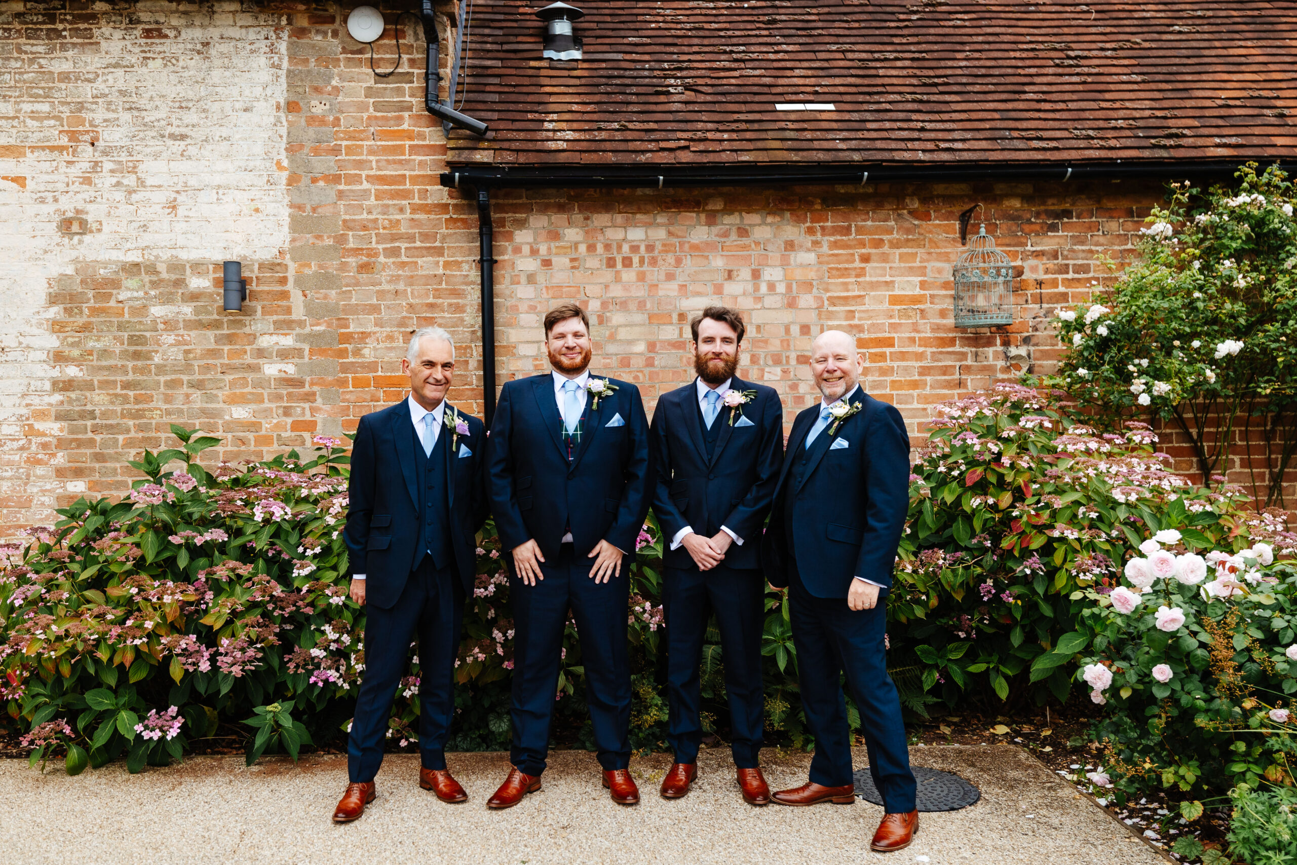 The groom and his groomsmen. They are in navy blue suits with pale blue ties and they have the same dark brown shoes on. They are all smiling and look very happy.