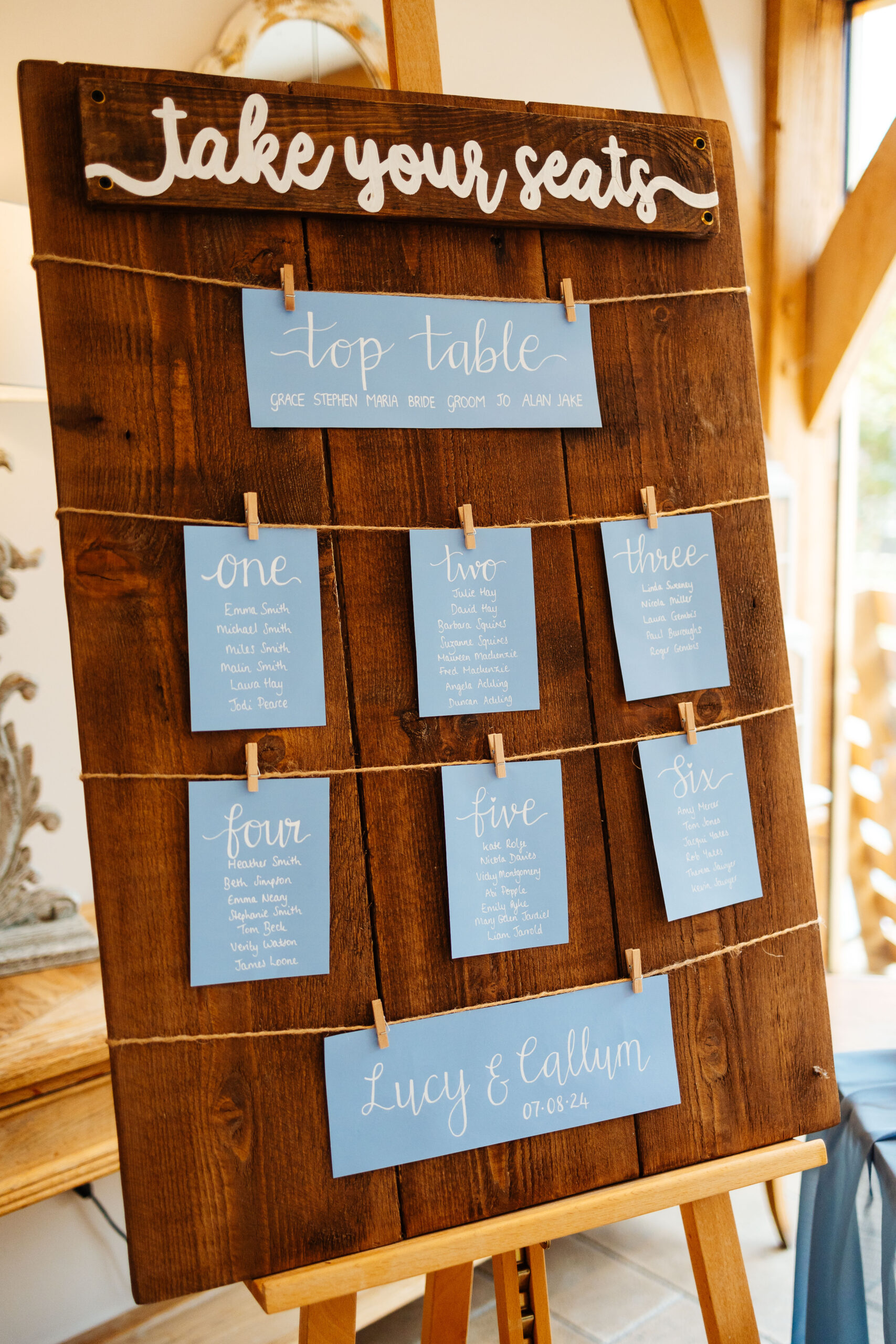 The table plan on 3 pieces of dark wood. The table plan is on blue card with white calligraphy writing on it and the table plan is hung on with pegs on string.