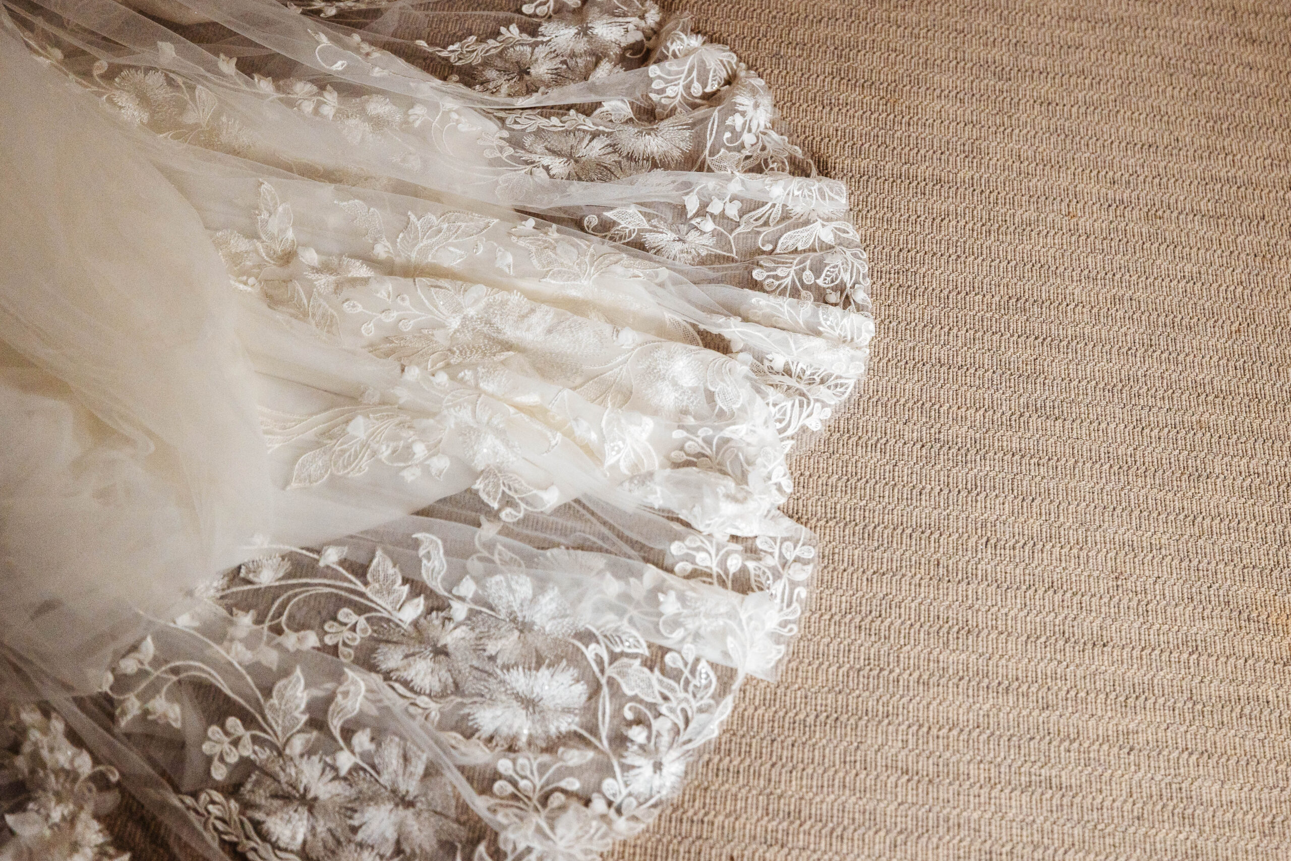 The bottom of the bride's dress to show its detail. She has lace detail on it showing little flowers and leaves in varying sizes.