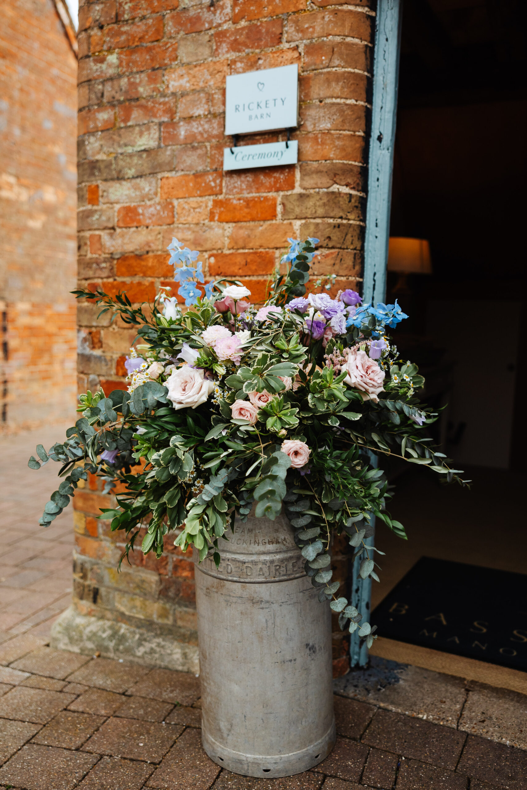 A huge bouquet of flowers in an old milk metal carton. They are pink and purple and have eucalyptus in it too.