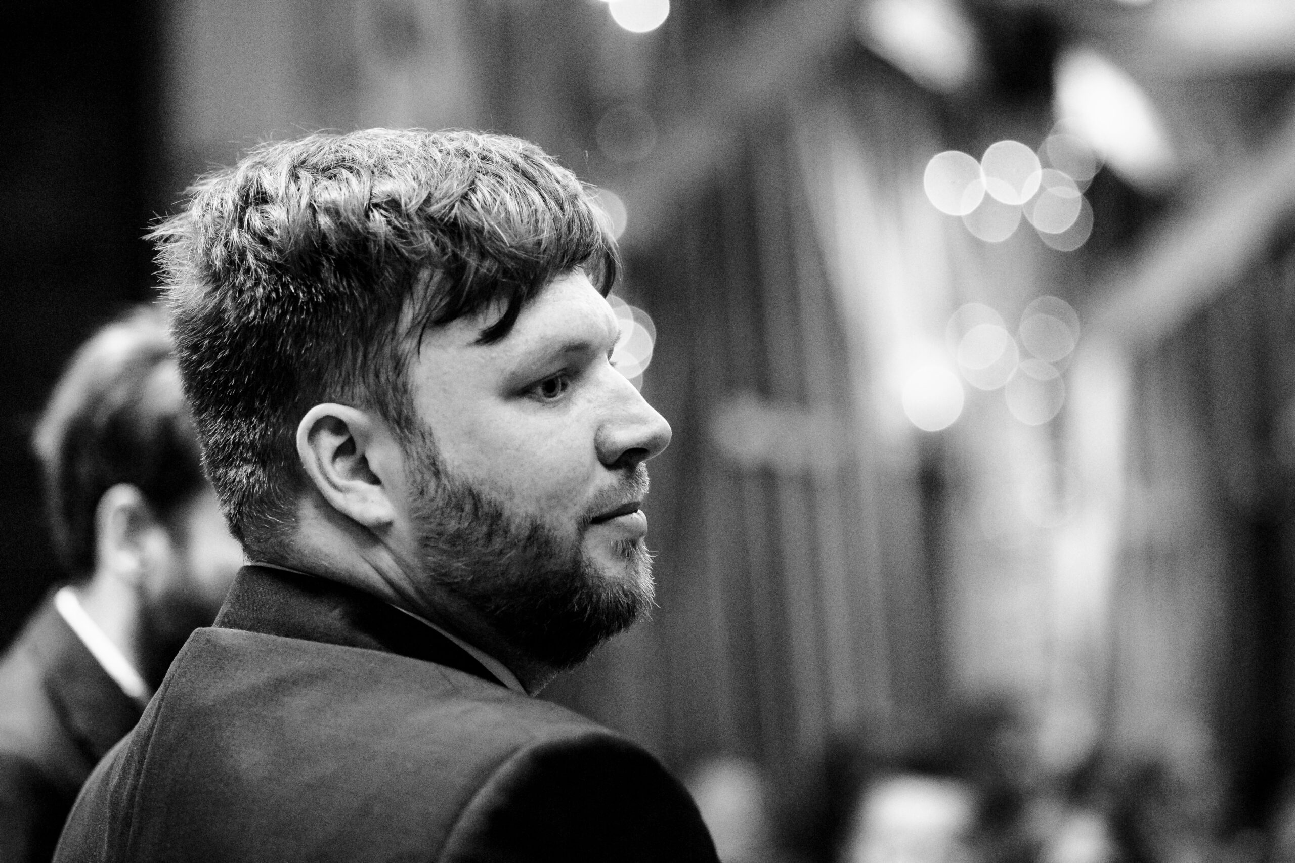 A black and white photo of the groom. He is at the top of the alter waiting for his bride. He looks nervous.