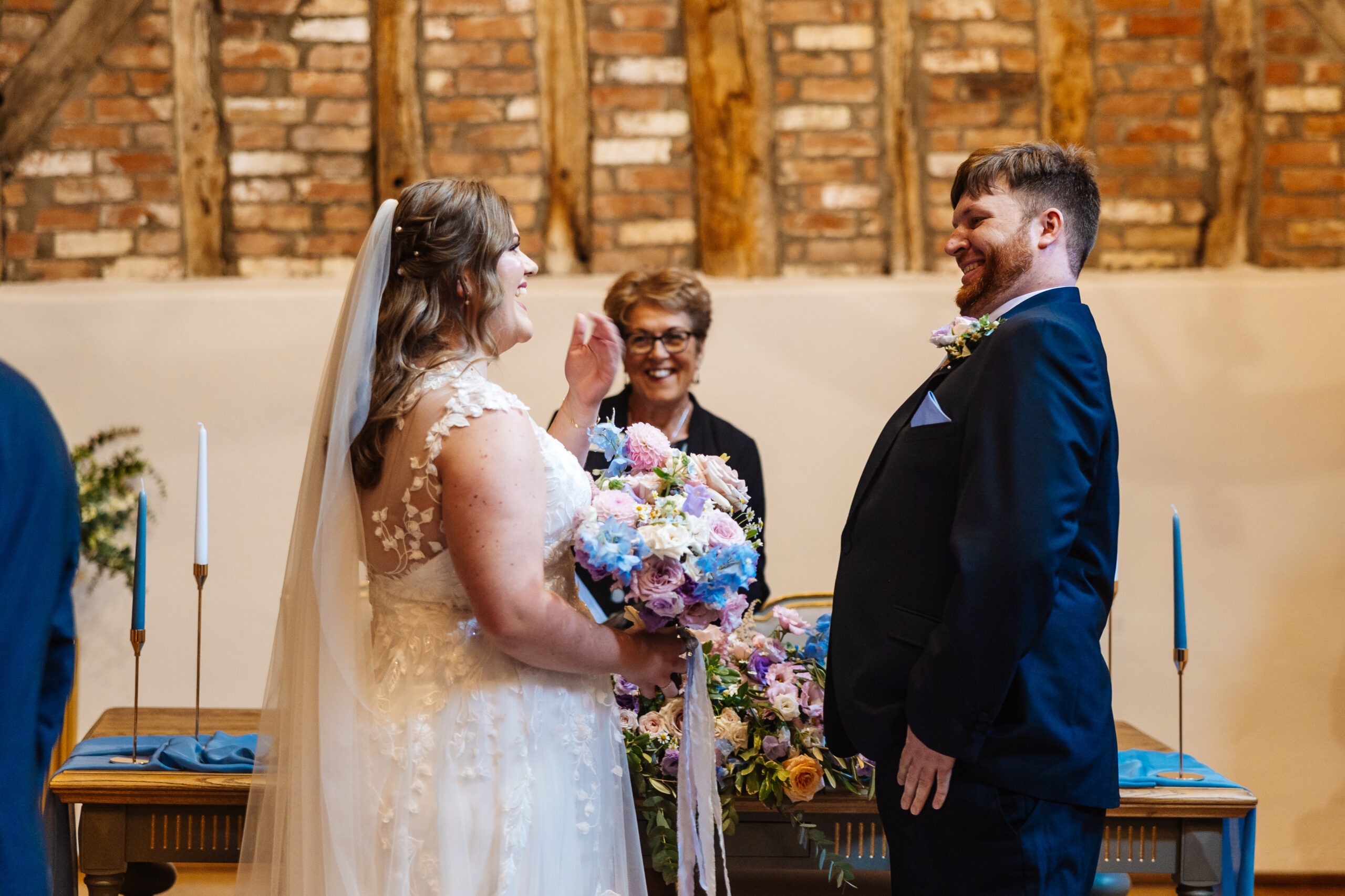 The bride and groom at the top of the alter. They are looking at each other and smiling. The celebrant is also smiling profusely. 