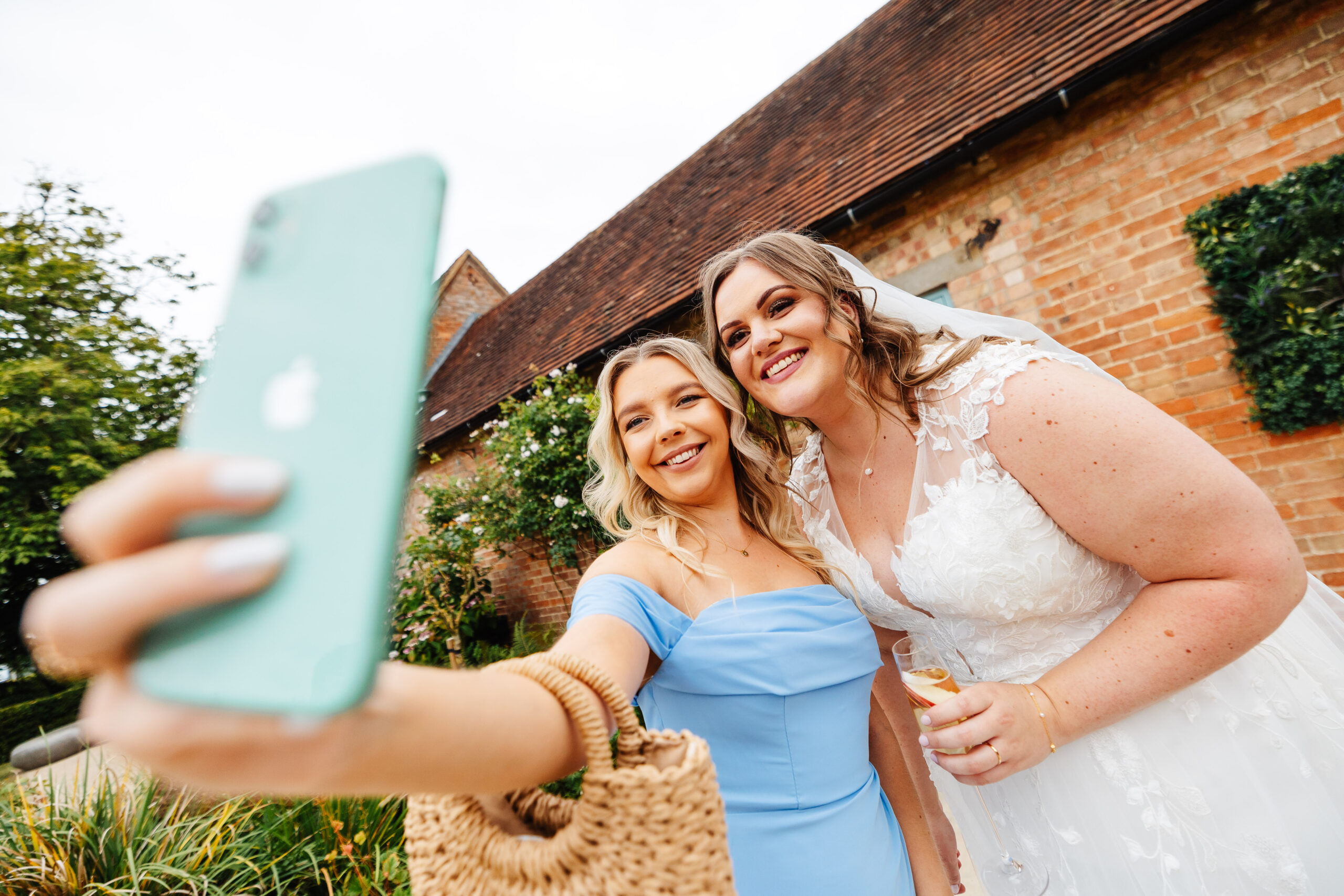 A photo of a bridesmaid and the bride taking a selfie. The bride is holding a glass of champagne.