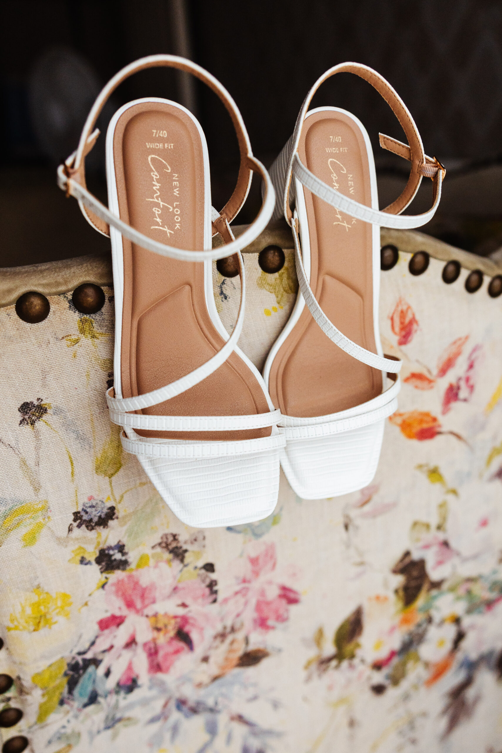 A pair of white, open toed heeled shoes. They have a strappy white strap over the toes that goes around the ankle.