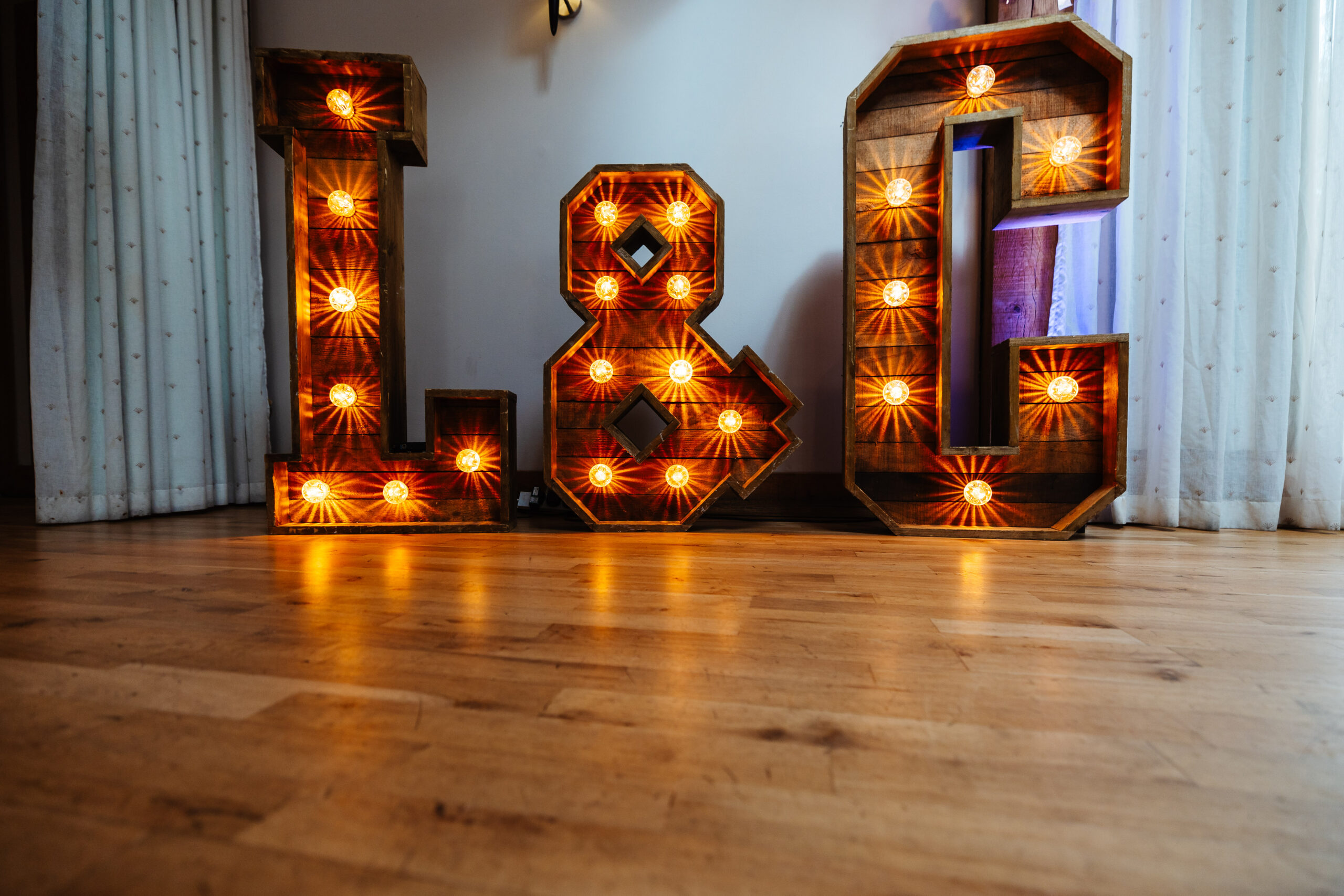 Large, light up letters with the letters L & C. The light bulbs are in the wooden letters and are shining on to the dance floor.