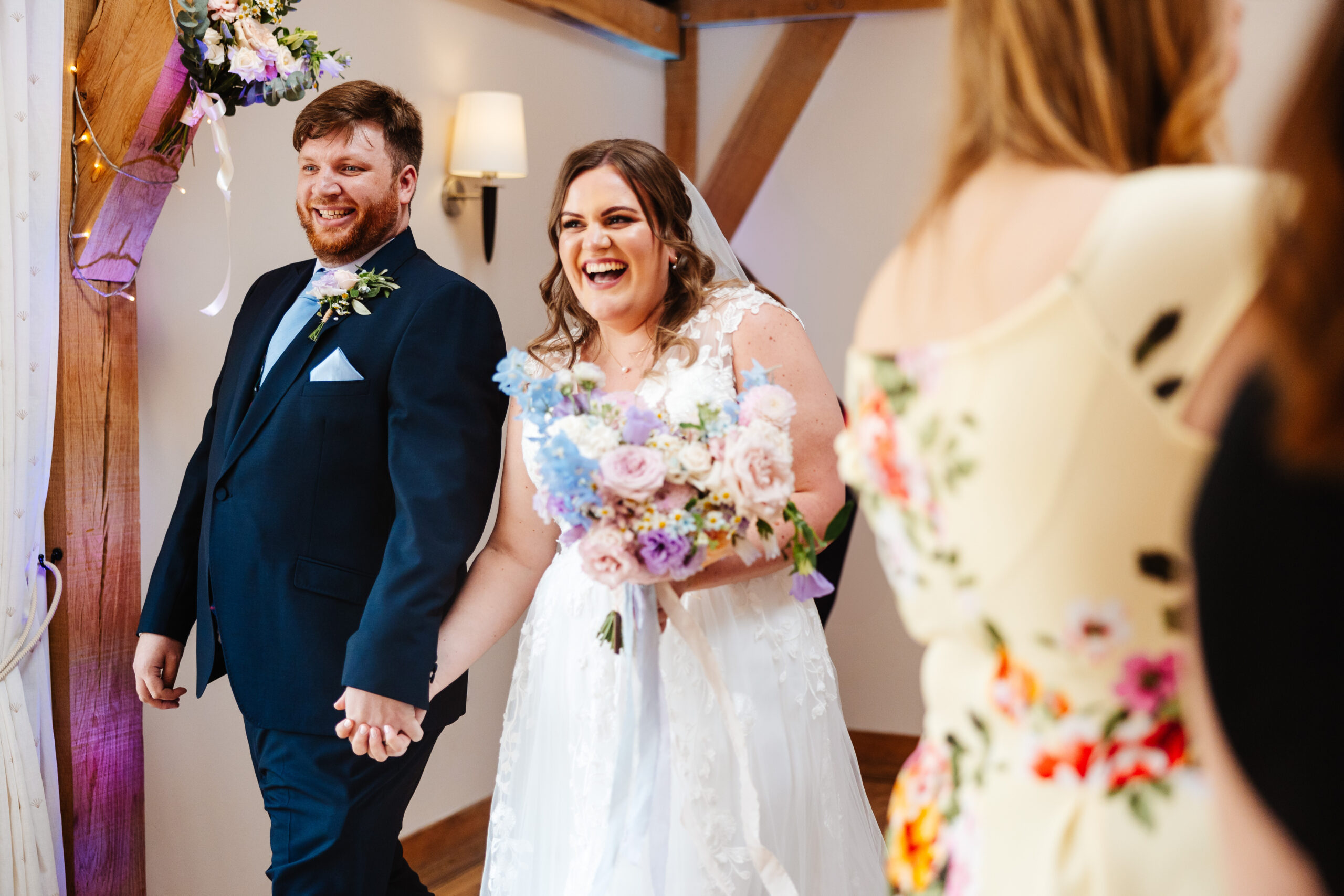 The bride and groom entering their wedding breakfast. They are walking hand in hand and are smiling looking at guests.