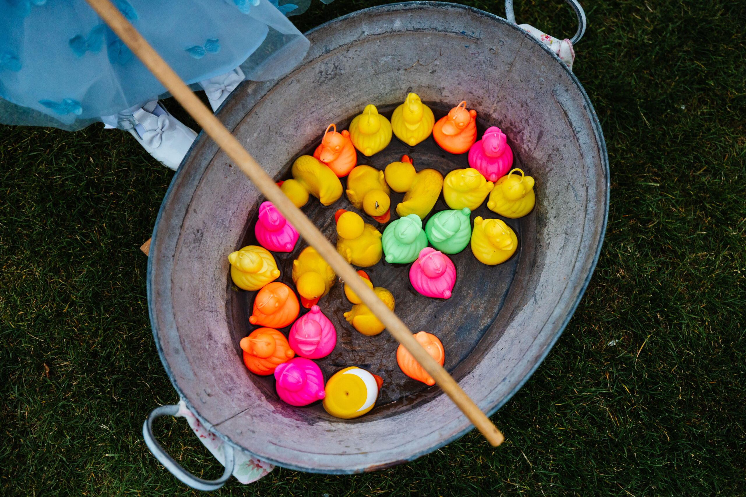 A metal container on the floor containing brightly coloured plastic ducks. There is a wooden stick above it depicting hook a duck.