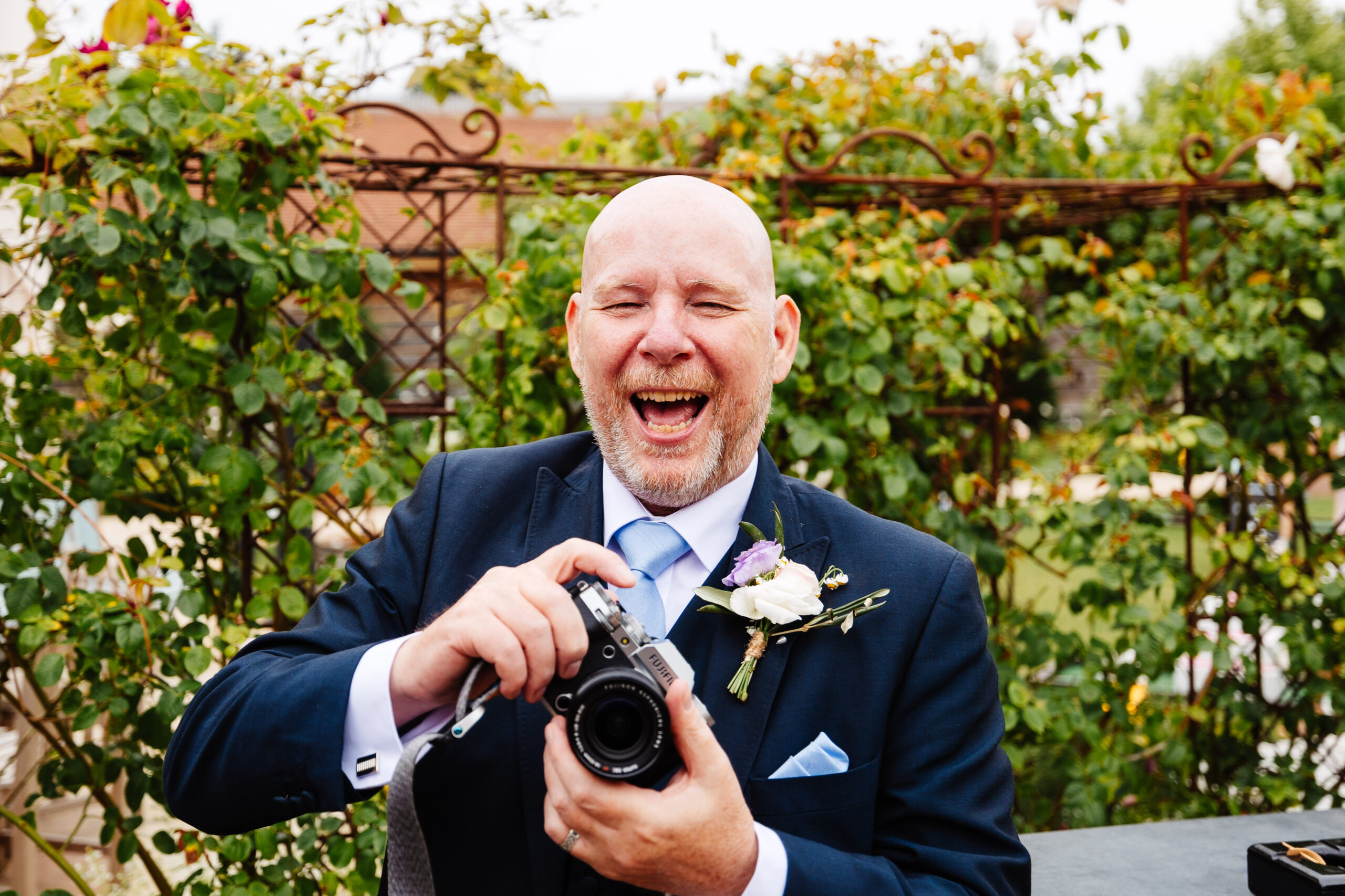 A photo of one of the groomsmen holding a professional camera. He is smiling and pointing the camera towards the cameraman!