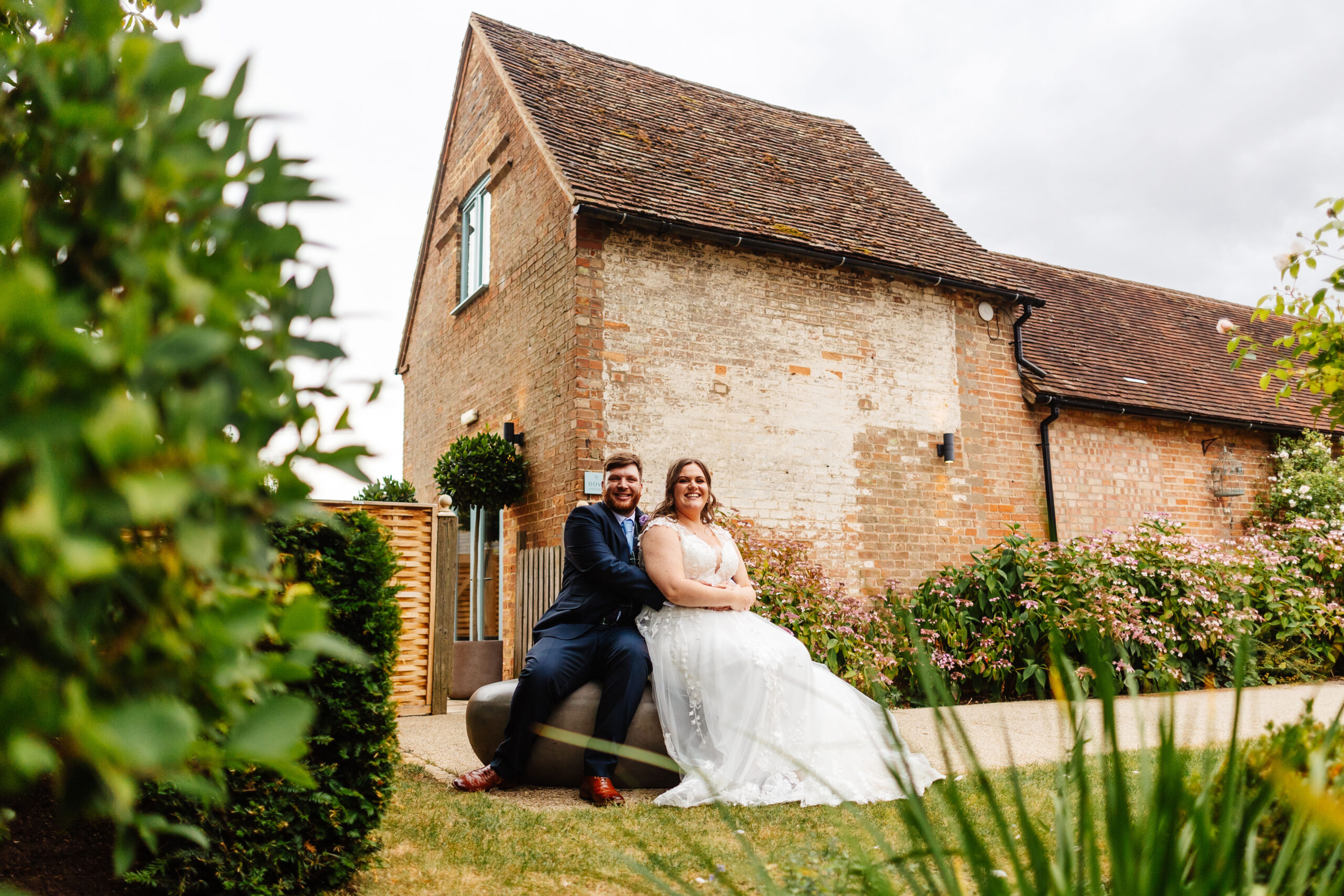 The bride and groom sat down on a bench in Bassmead Manor gardens. You can see the lush gardens in the background.